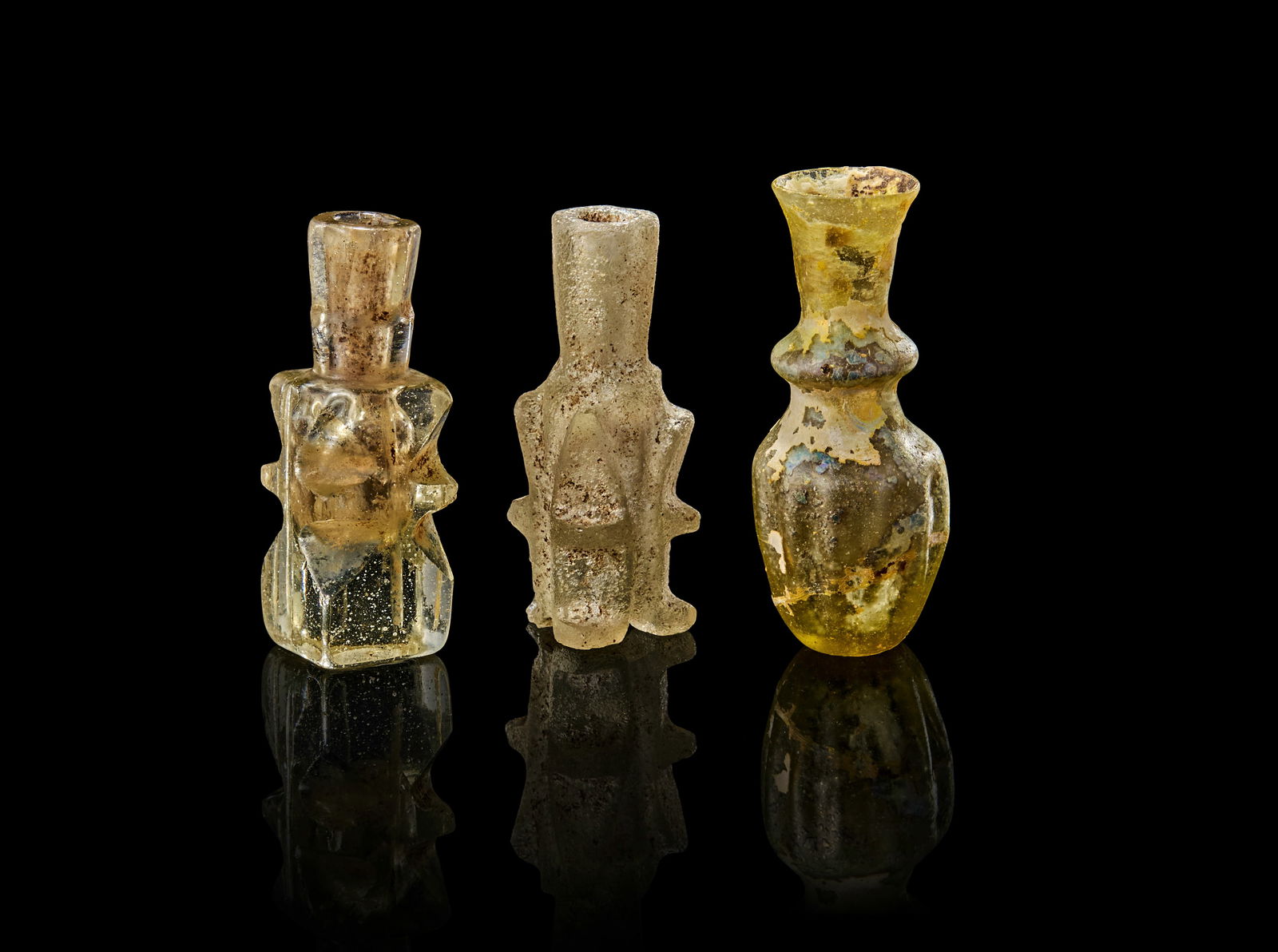 A TWO FATIMID GLASS MOLAR FLASK AND ANCIENT PERSIAN GLASS, 11TH - 12TH CENTURY: The molar flasks feature angular, multi-lobed bodies with cylindrical necks, while the Persian piece exhibits a more rounded. Tallest 6.5 cm 