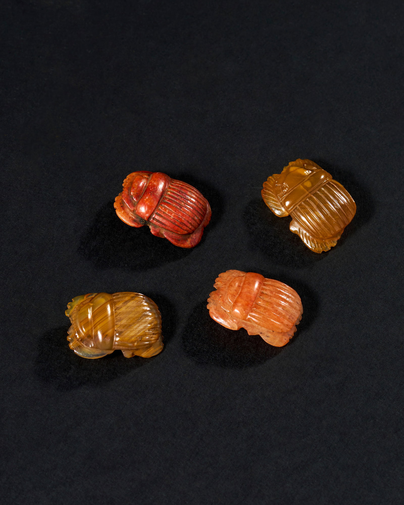 A COLLECTION OF EGYPTIAN AGATE SCARAB, LATE PERIOD, 664 - 323 B.C.: This fascinating collection comprises four intricately carved scarabs, each crafted from various shades of agate, dating from the Late Period of ancient Egypt (664-323 B.C.). The scarab beetle was a p