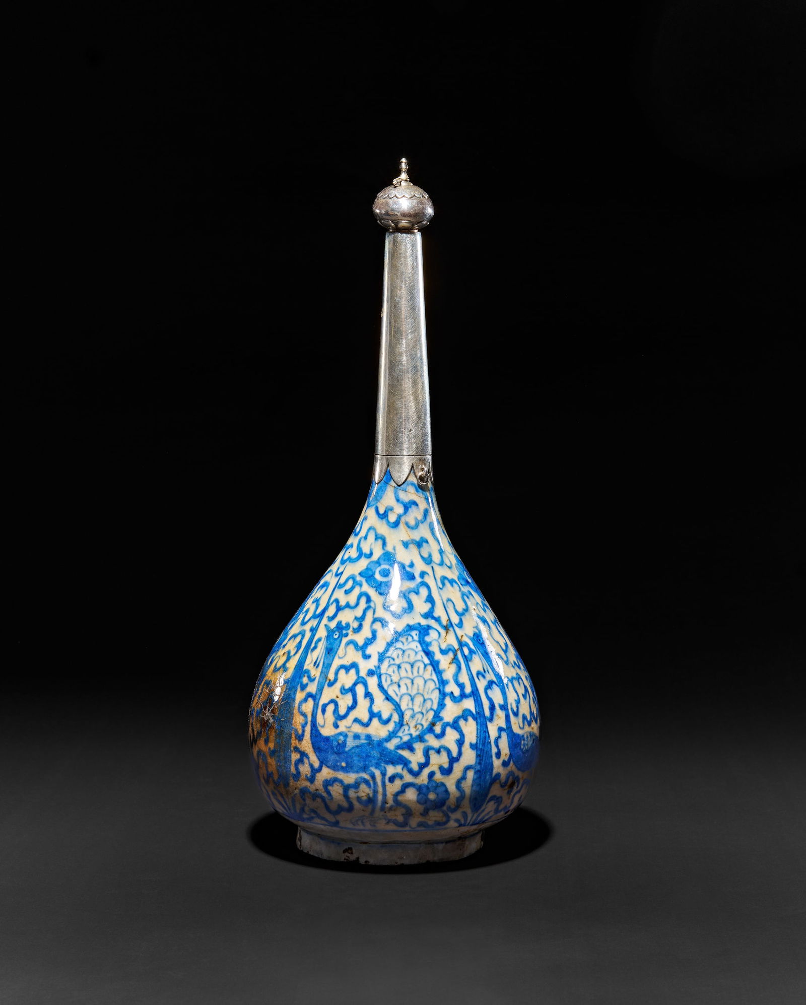 A BLUE AND WHITE SAFAVID GLAZED POTTERY SURAHI BOTTLE, PERSIA, 16TH - 17TH CENTURY: A large fine 16-17th century early Safavid Persian blue and white glazed pottery bottle (surahi) flask depicting peacocks and cypress trees amongst cloud bands, silver neck is a later 19-20th century