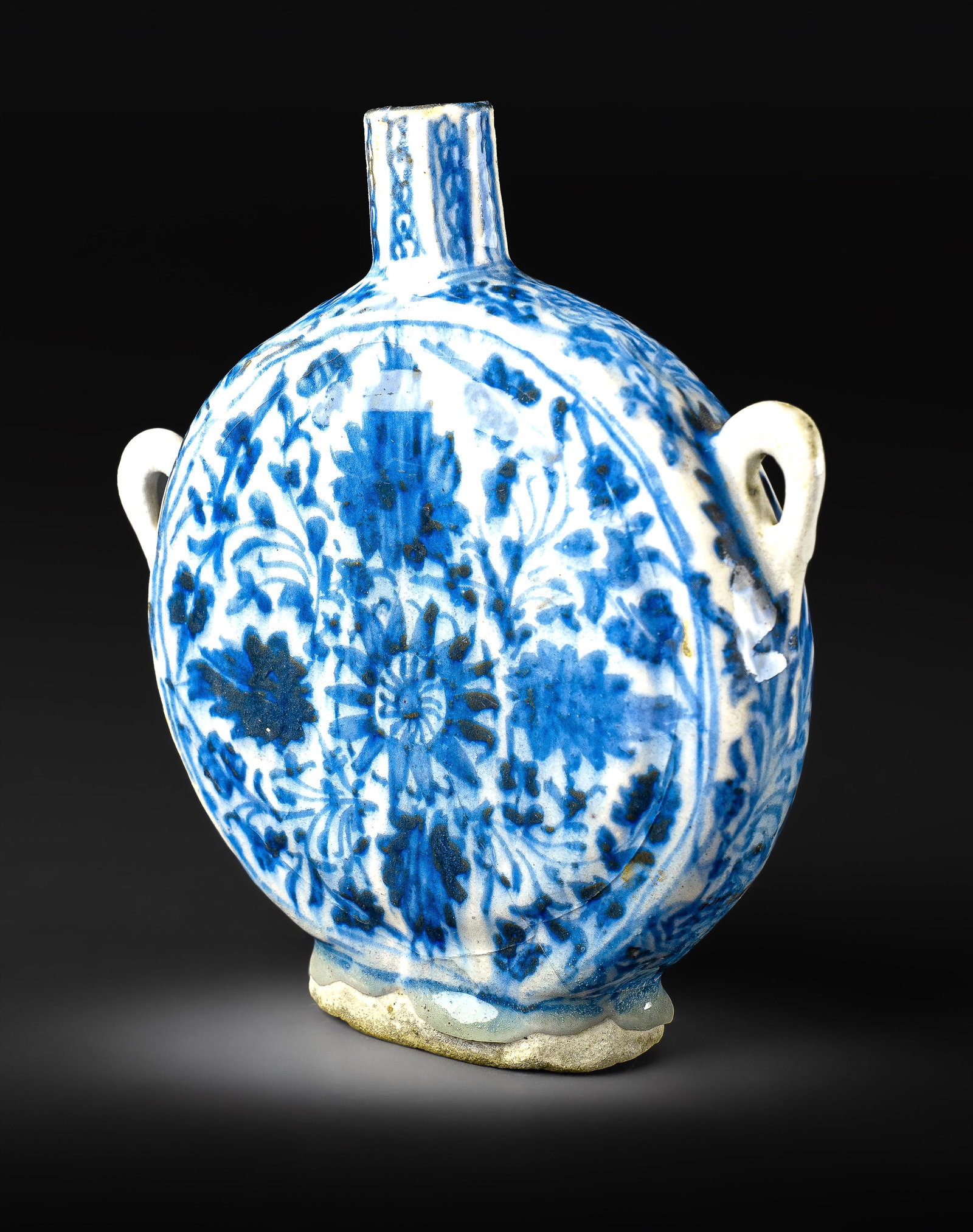 A BLUE AND WHITE SAFAVID POTTERY MOON FLASK, PERSIA, 17TH CENTURY: Of circular flattened form with a short cylindrical neck and twin strap handles, the flask is painted in underglaze cobalt blue with a bold central medallion of floral sprays, surrounded by dense scro