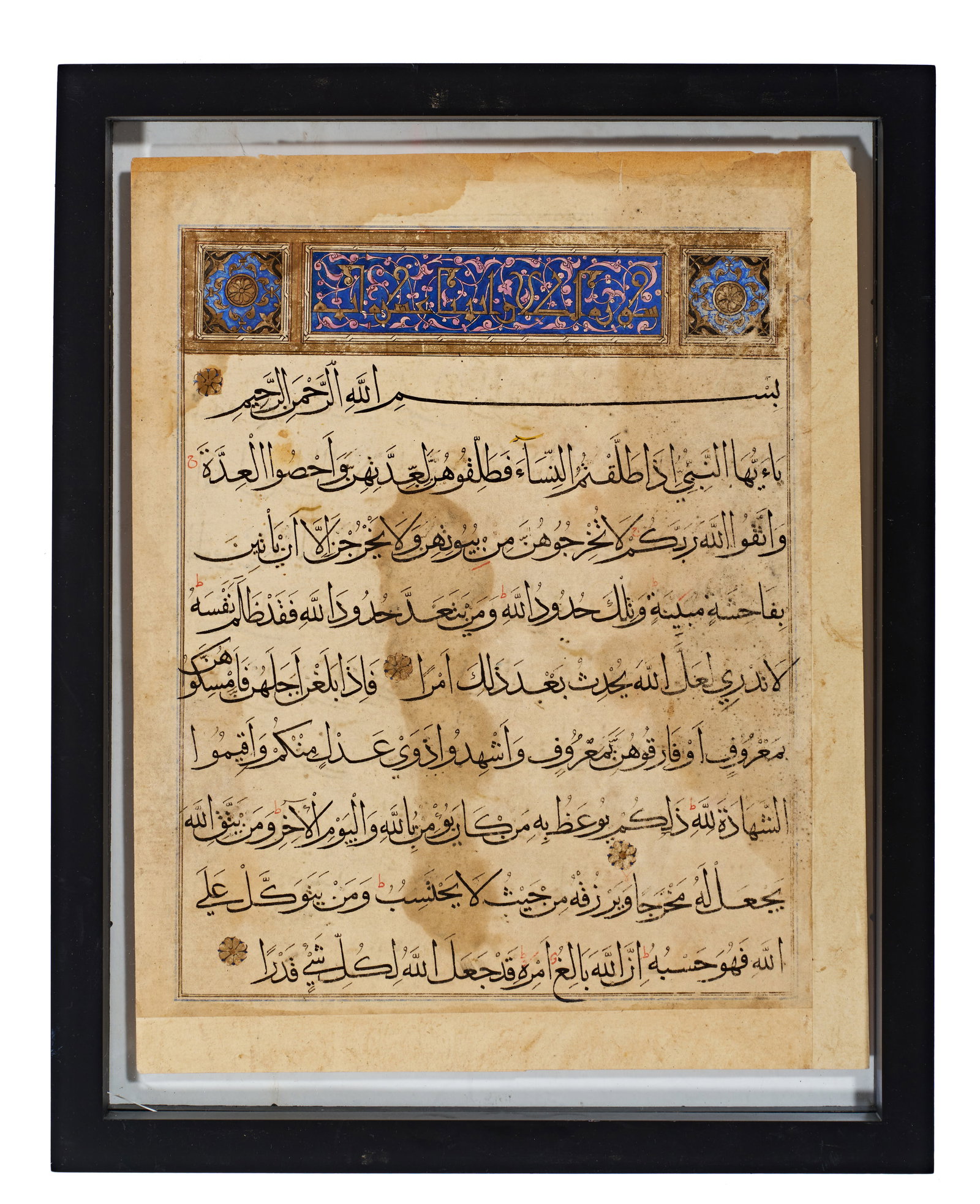 AN ILLUMINATED TIMURID QURAN MANUSCRIPT PAGE, PERSIA, 15TH CENTURY: One side presents an illuminated heading for Surat al-Talaq (Chapter of Divorce), executed in blue, gold, and pink pigments with floral and geometric motifs. The text includes the Basmala and is punct