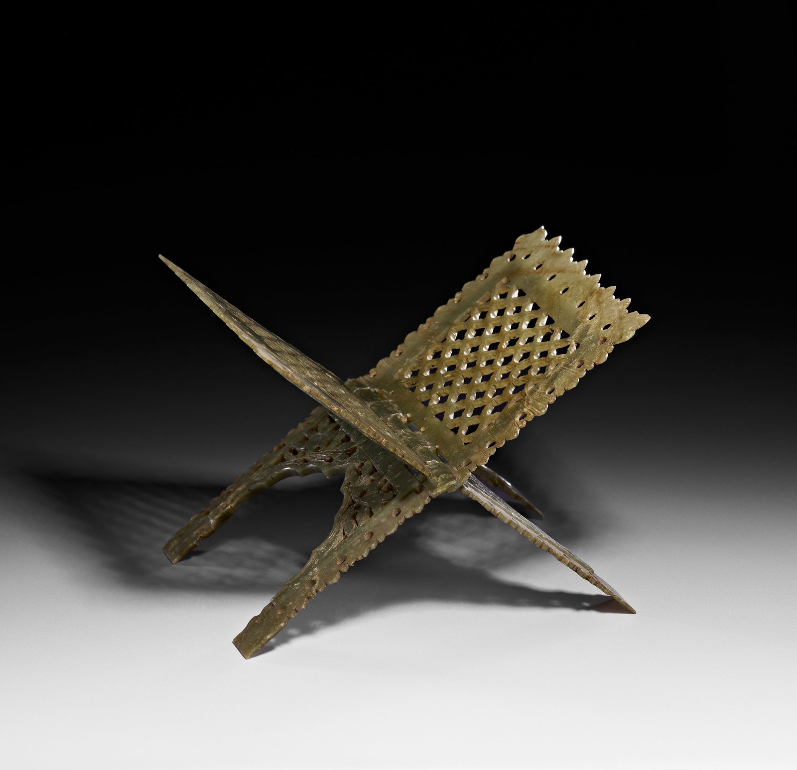 AN INDIAN CARVED JADE QURAN STAND MARUFAA, MUGHAL, 18TH - 19TH CENTURY: This Indian carved jade quran stand, also known as a marufaa, is constructed from two interlocking, hinged panels that open to form an X-shaped cradle. The object is carved from mottled pale green jad