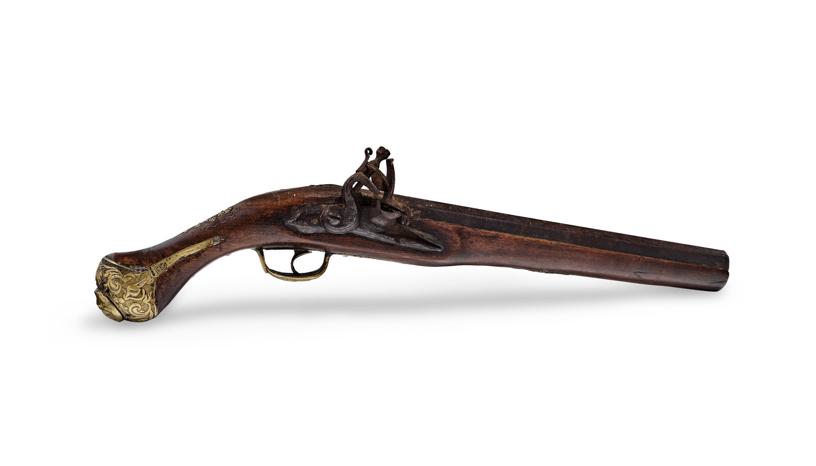 AN OTTOMAN FLINTLOCK PISTOL, TURKEY, 19TH CENTURY: This Ottoman flintlock pistol features a dark wood stock with ornate brass furniture. The iron barrel is octagonal at the breech and transitions toward the muzzle. The flintlock mechanism is construct