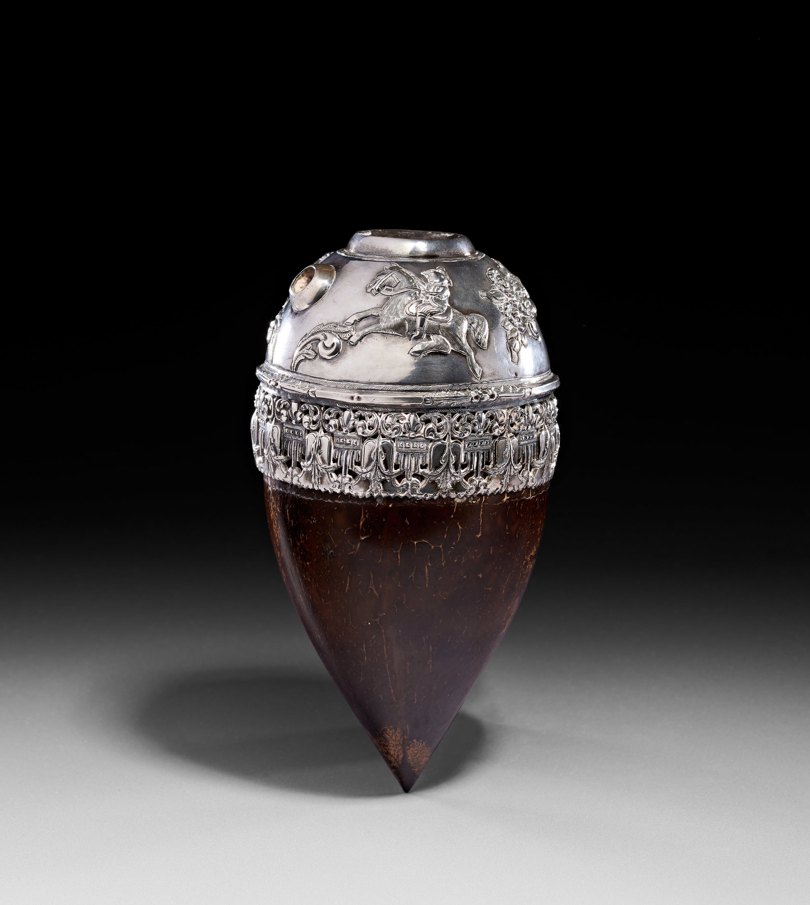 A SILVER-MOUNTED COCONUT SHELL HUQQA BASE, QAJAR, 19TH CENTURY: This Huqqa Base consists of a polished, dark brown ovoid coconut shell tapering to a point. The vessel is fitted with silver mounts, including a domed top and a wide mid-band. The silver top fea
