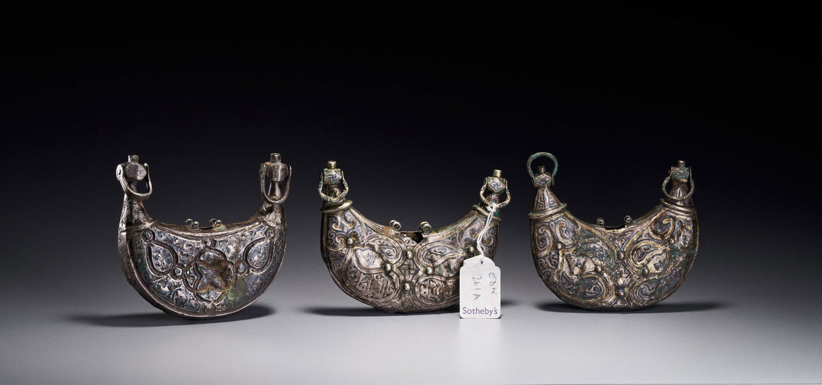 A THREE SELJUK SILVER AND NIELLO PECTORAL AMULET CASES, IRAN, CIRCA 12TH CENTURY: Comprising three crescent-shaped silver amulet cases with niello decoration, each one hollow inside and with tapering terminals with circular hoops, the silver sheet hammered, engraved and nielloed, t