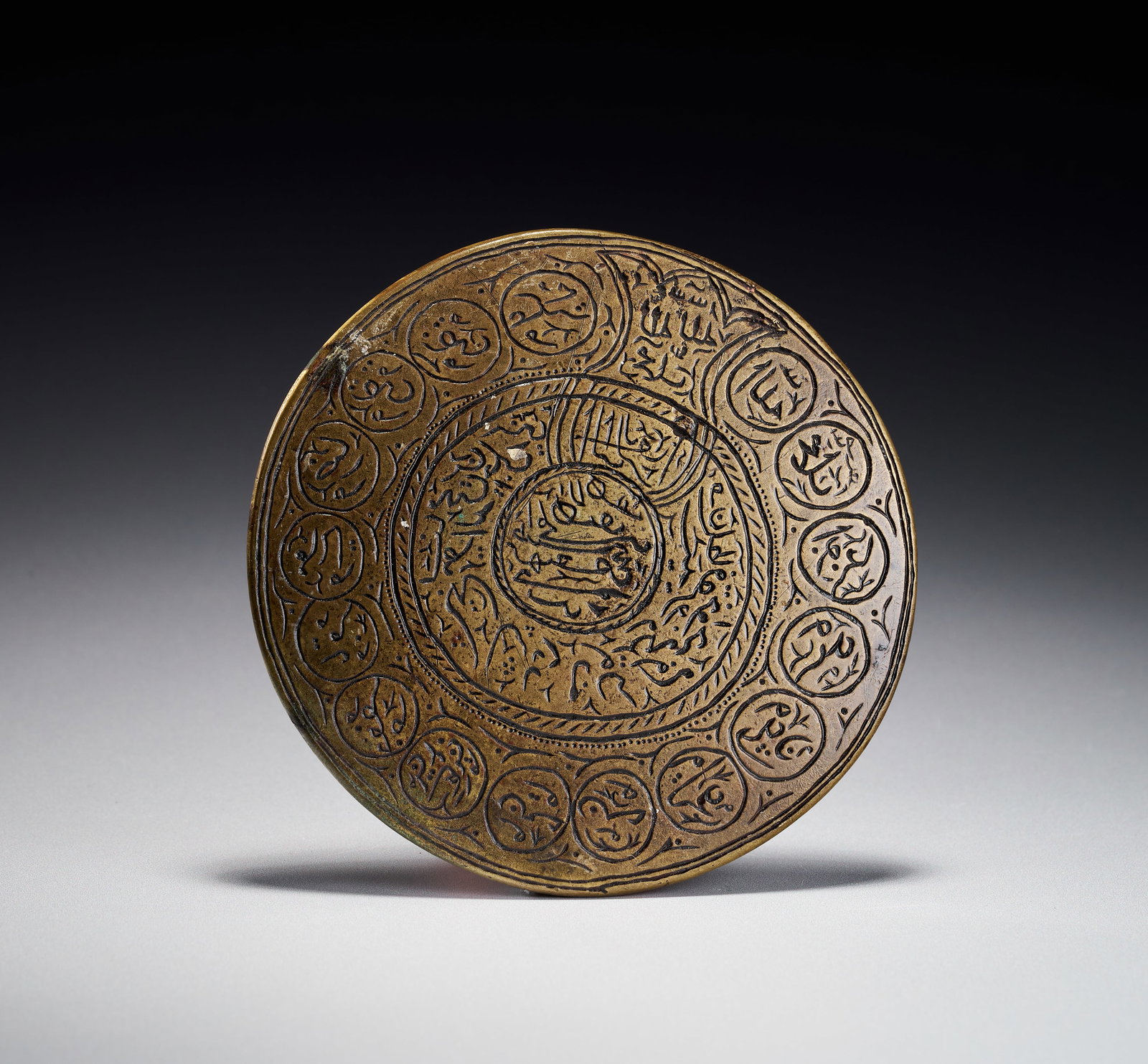 A PERSIAN ENGRAVED BRASS TALISMANIC PLAQUE WITH THE NAMES OF THE TWELVE IMAMS, 19TH CENTURY (1 of 2)