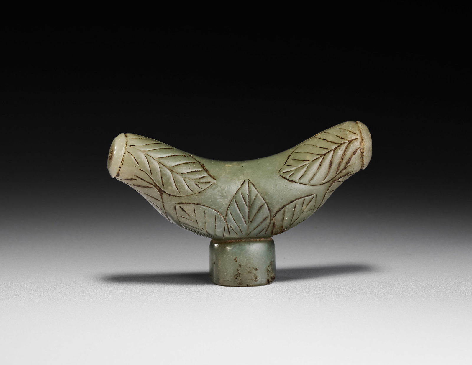 A DERVISH CRUTCH MUGHAL JADE HANDLE FOR THE OTTOMAN MARKET, INDIA, 18TH CENTURY: This carved pale green stone handle, possibly nephrite jade, is fashioned in a crescent form characteristic of a crutch handle, or zafar-takiya, in the Mughal or North Indian style. The body features