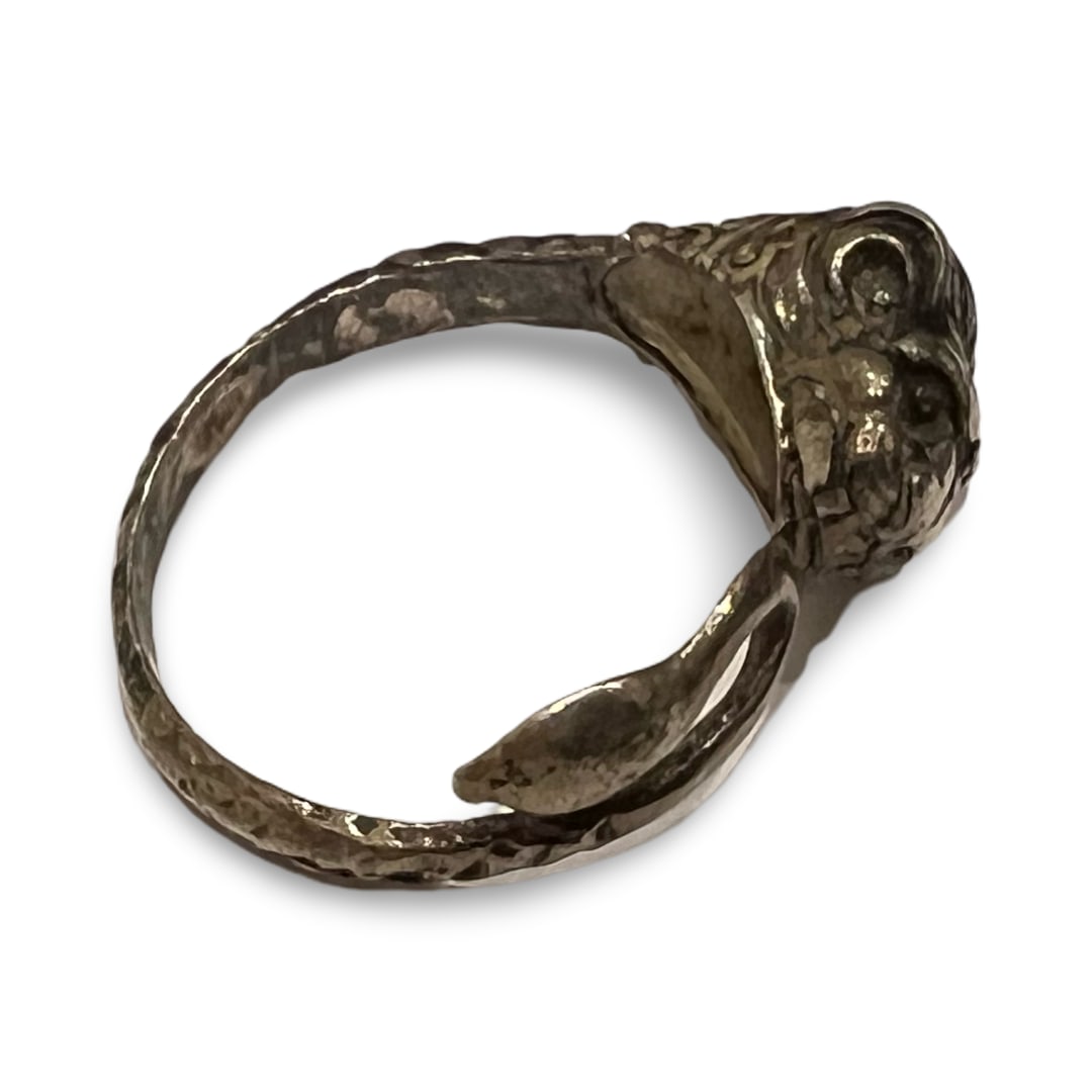 A SILVER TONED LION HEAD FIGURAL RING: This sculptural figural ring is composed of a white metal, appearing to be silver or a silver-toned alloy. The design features a central three-dimensional stylized feline head, likely a lion, with tex
