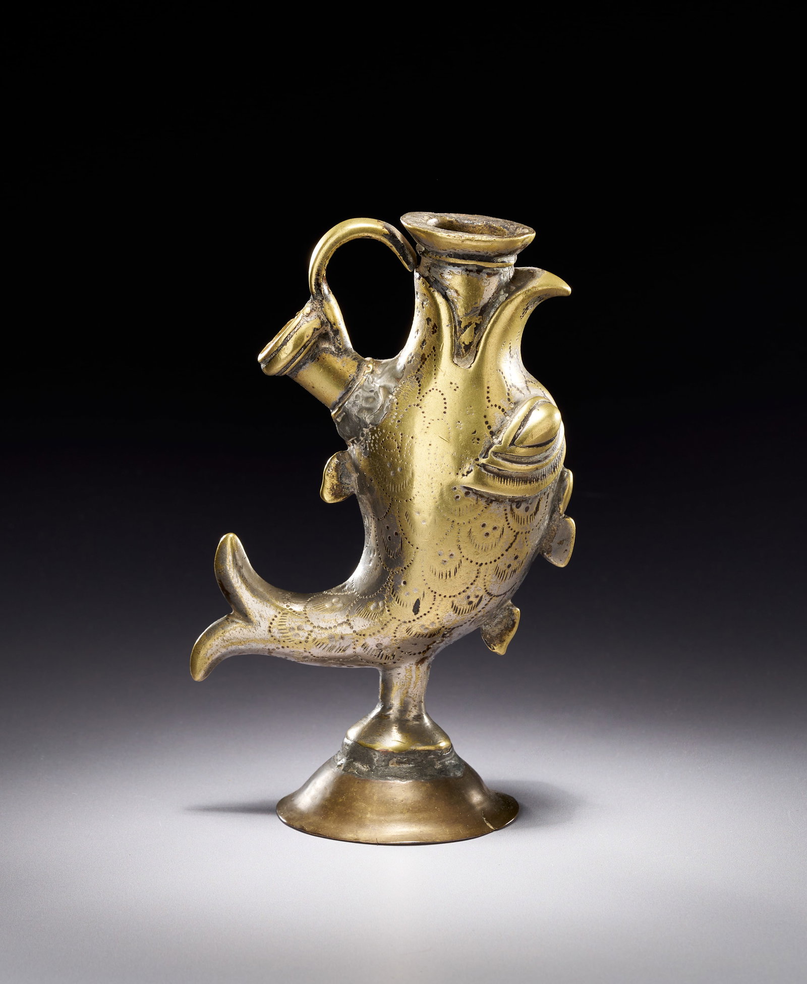 AN INDO-PERSIAN SILVERED BRASS ZOOMORPHIC VESSEL IN THE FORM OF A FISH: This silvered brass zoomorphic vessel is fashioned in the form of a stylised upright fish, likely originating from Northern India or Iran during the 18th or 19th century. The piece features a central 