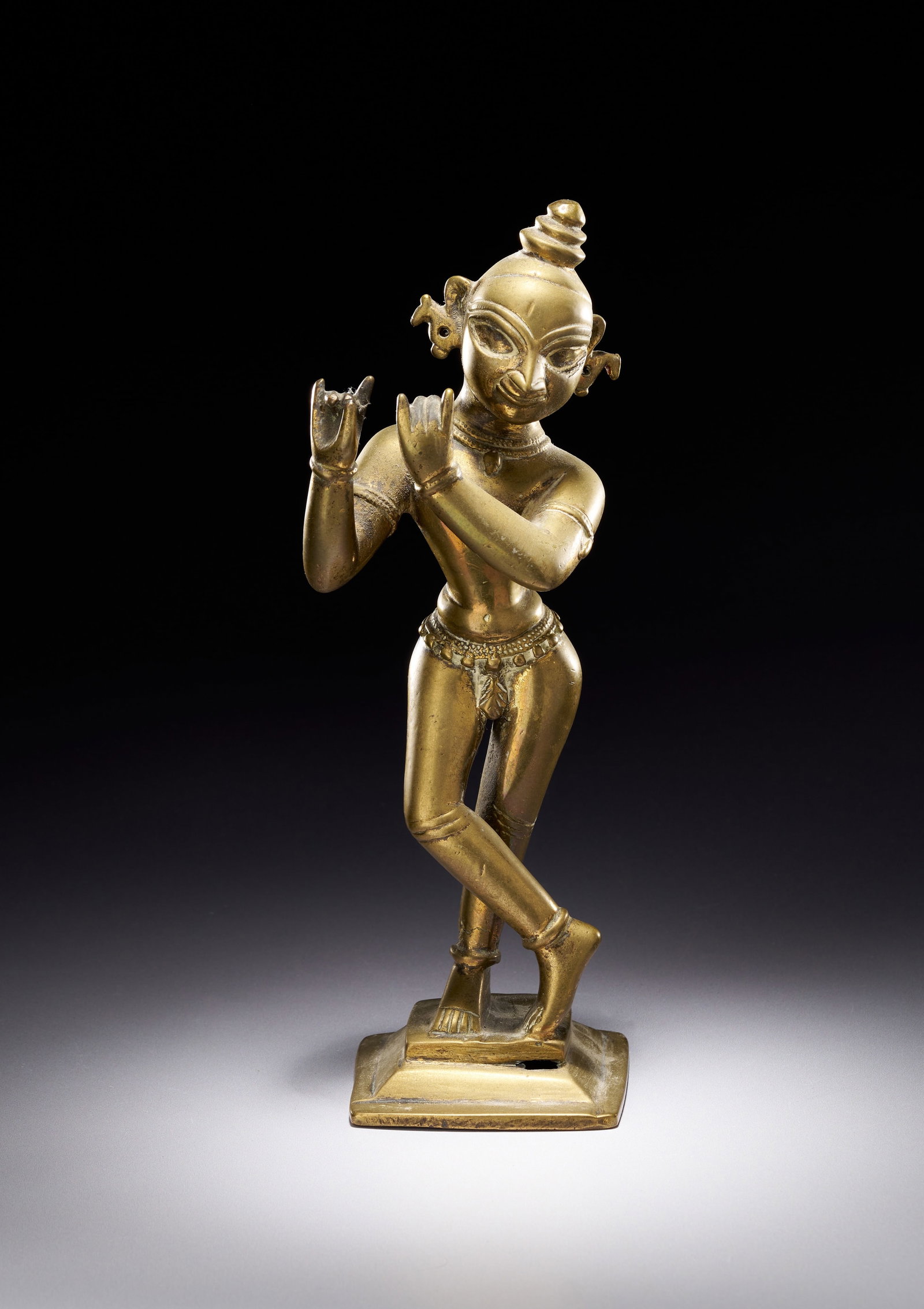 INDIAN CAST COPPER ALLOY FIGURE OF KRISHNA VENUGOPALA: An Indian cast copper alloy figure, likely brass, depicting the Hindu deity Krishna in the form of Venugopala. The sculpture is executed in a provincial folk style characteristic of the Odisha region,