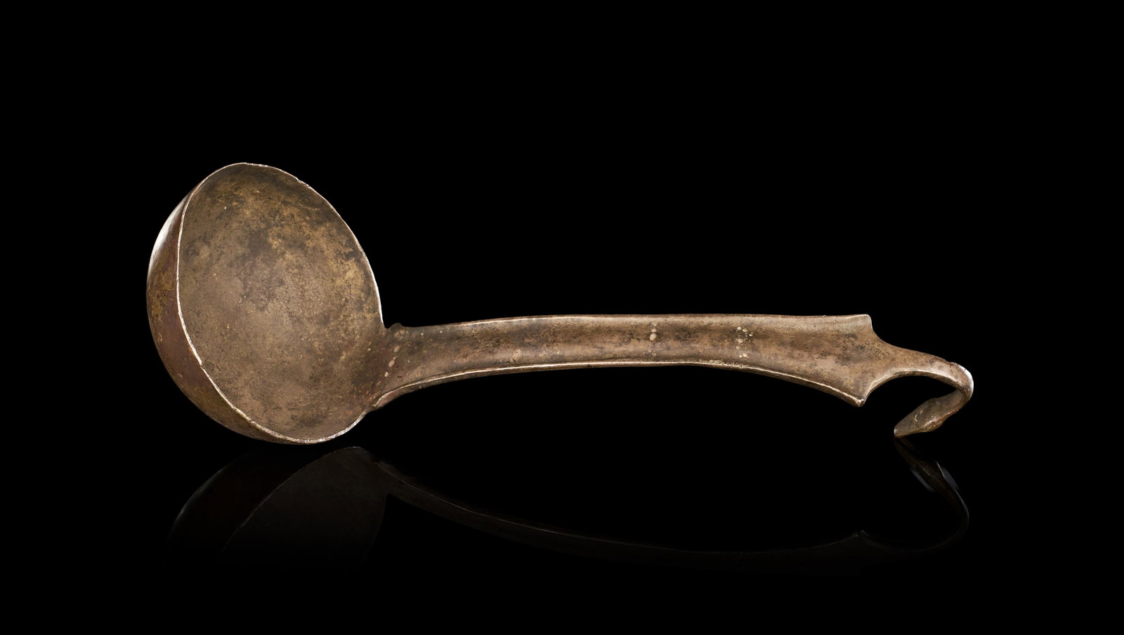 AN ANCIENT ROMAN CAST BRONZE LADLE WITH ZOOMORPHIC TERMINAL: A cast copper alloy ladle of classical form, consistent with Roman provincial metalwork. The object features a deep hemispherical bowl joined at a right angle to a long, tapering flat handle. The hand