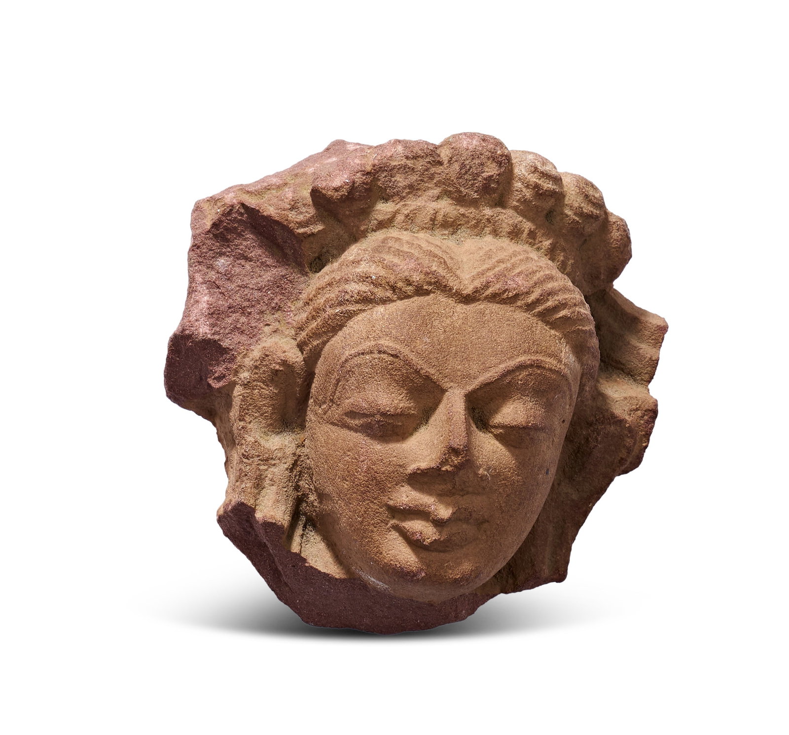 A RED SANDSTONE HEAD OF A FEMALE DEITY, CENTRAL INDIA, MATHURA, CIRCA 2ND CENTURY: his fragmentary carved head of a female deity or celestial being, such as a yakshi or apsara, is sculpted from mottled red Sikri sandstone. Originating from the Mathura region of India, the piece repr