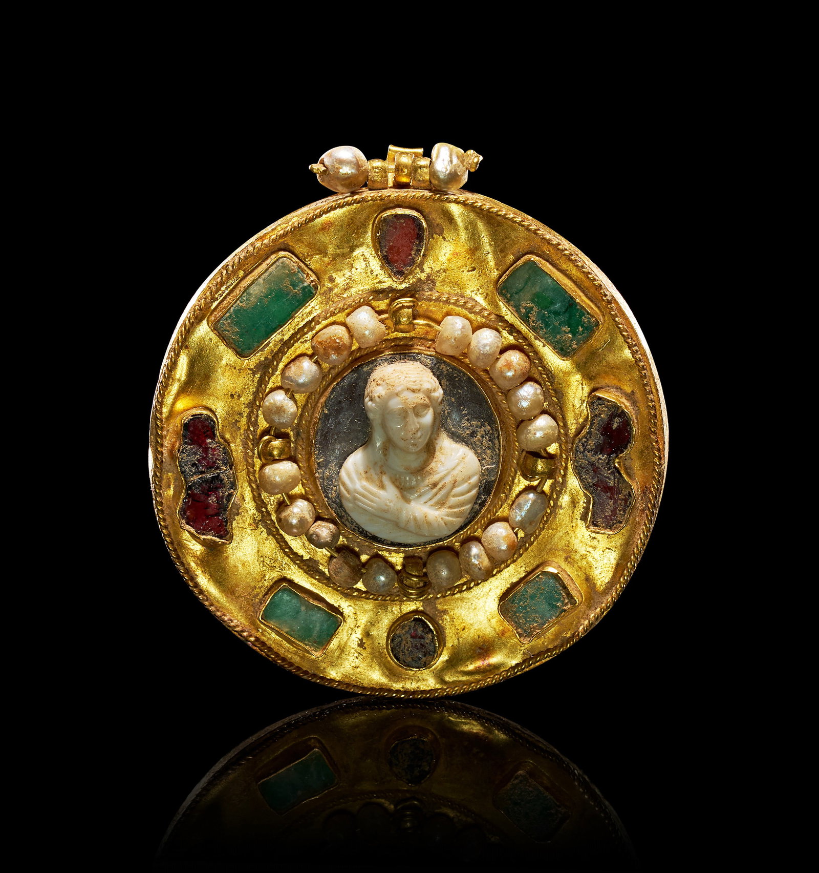 A RARE ROMAN GOLD PENDANT SET WITH A CENTRAL CAMEO, PEARLS, AND GEMSTONES, 1ST - 2ND CENTURY A.D: Featuring a central hardstone cameo carved in relief with a classical-style bust of a youthful figure. The cameo is set within a ring of small, graduated seed pearls. This central arrangement is mount