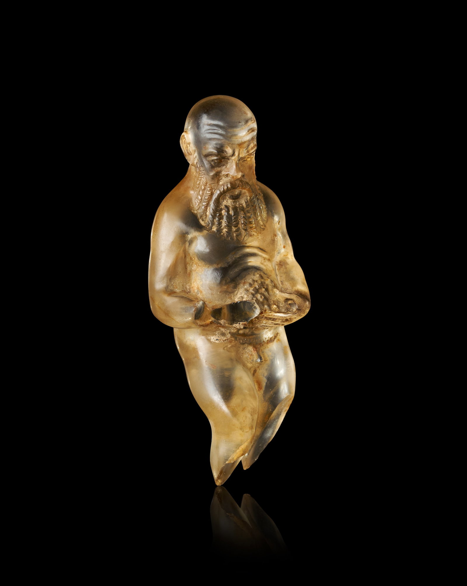 A RARE ROMAN CARVED QUARTZ FIGURINE OF A BEARDED MAN, 2ND - 3RD CENTURY A.D.: This carved gemstone figurine, fashioned from a translucent quartz such as citrine or smoky quartz, depicts a kneeling, bearded male figure. Dating to the 2nd to 3rd Century A.D., the work is executed