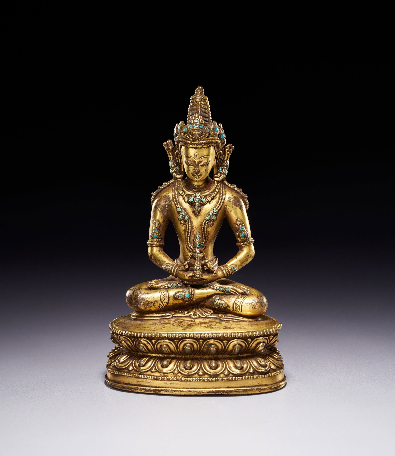 A TIBETAN GILT-BRONZE FIGURE OF AMITAYUS, 18TH CENTURY: The deity is seated in dhyanasana (meditative posture) upon a double-lotus pedestal featuring beaded upper and lower borders. The hands are positioned in dhyana mudra (gesture of meditation) in the la