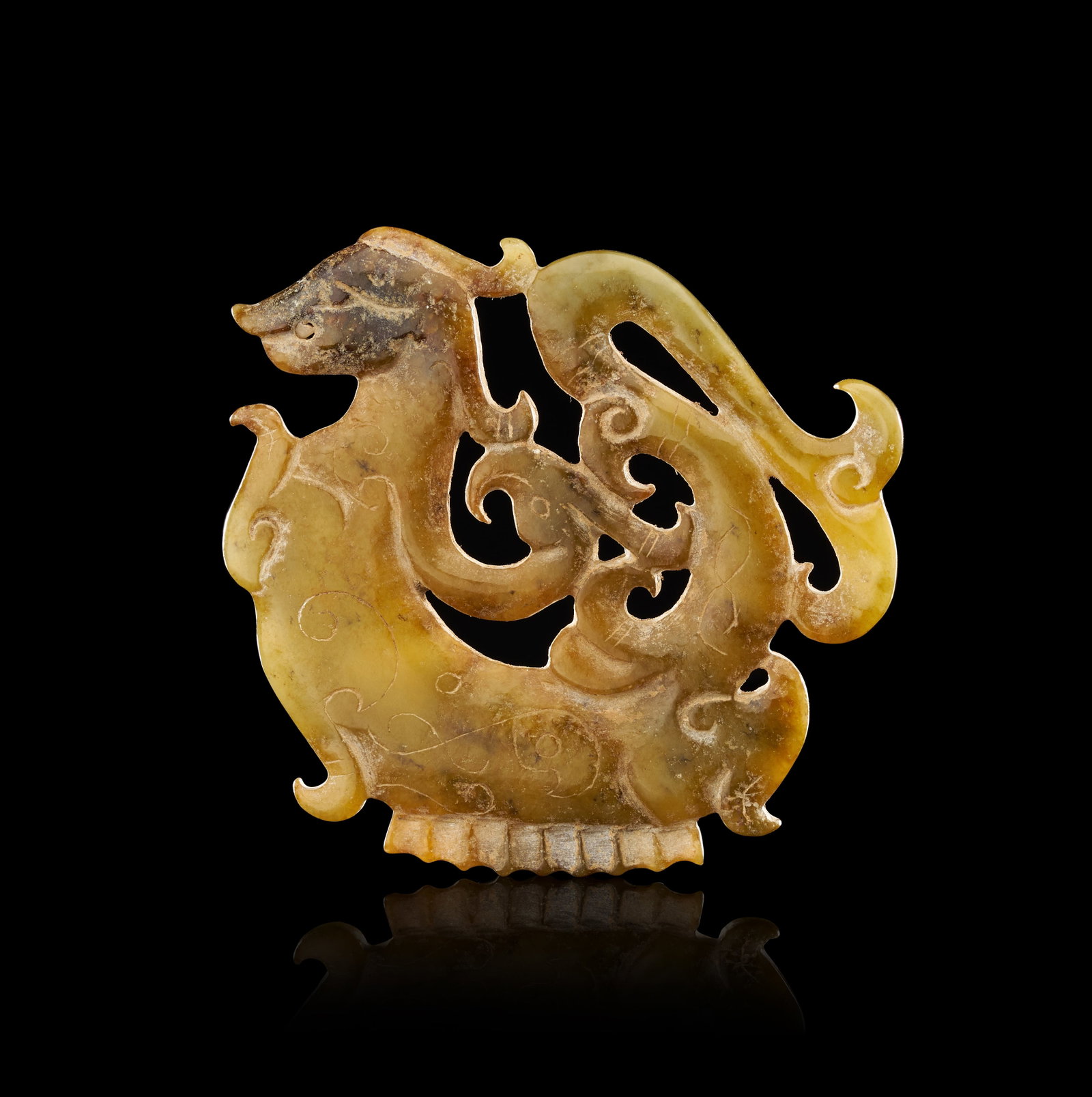 A CHINESE ARCHAIC STYLE RETICULATED JADE PLAQUE OF A MYTHICAL BEAST: A Chinese nephrite jade plaque carved in openwork from a stone of yellowish-celadon colour featuring dark brown and russet inclusions. The piece depicts a mythical beast, possibly a bixie, rendered in