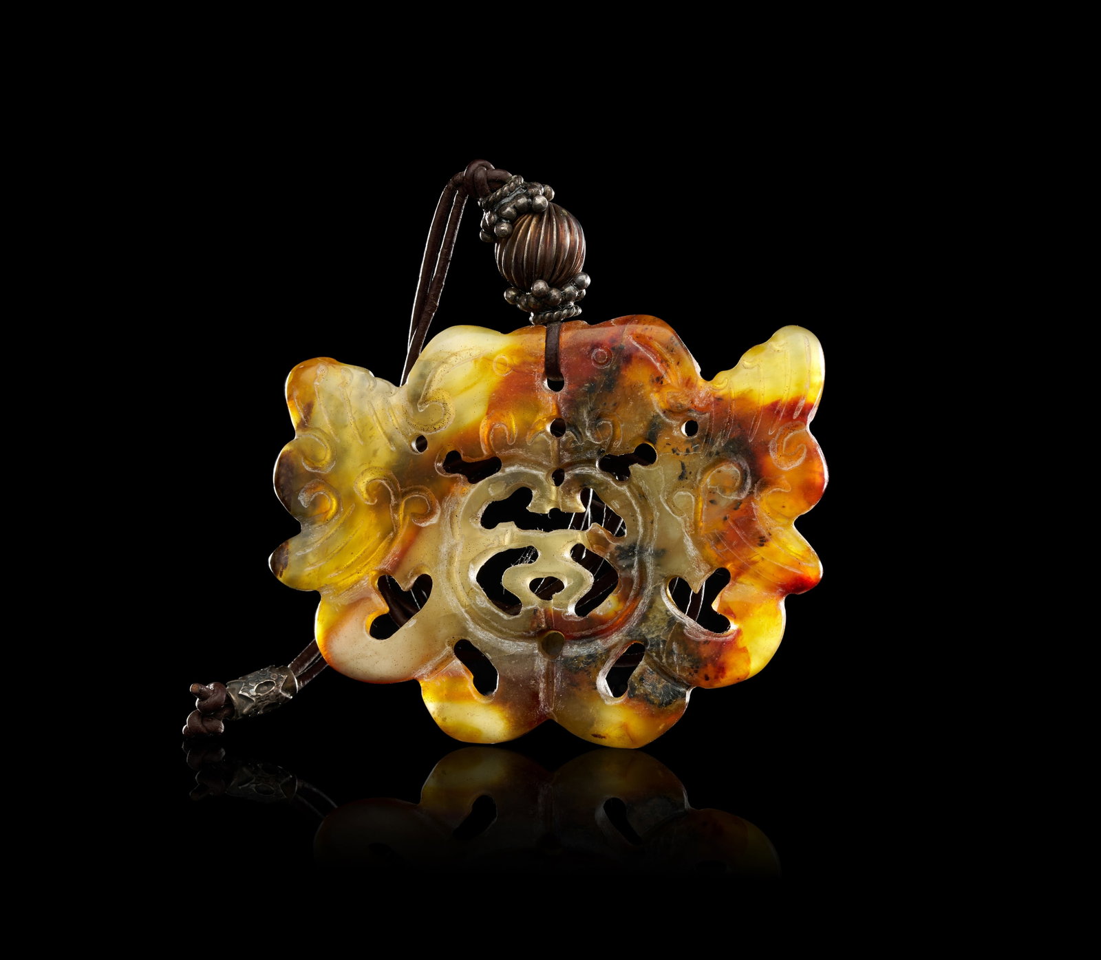 A CHINESE TRI-COLOUR NEPHRITE JADE SHOU CHARACTER BAT PENDANT, LATE 19TH - EARLY 20TH CENTURY: A Chinese carved nephrite jade pendant of lobed form, mounted on a dark brown cord, dating to the late 19th or early 20th century. The stone is of variegated tri-colour appearance, featuring transluce