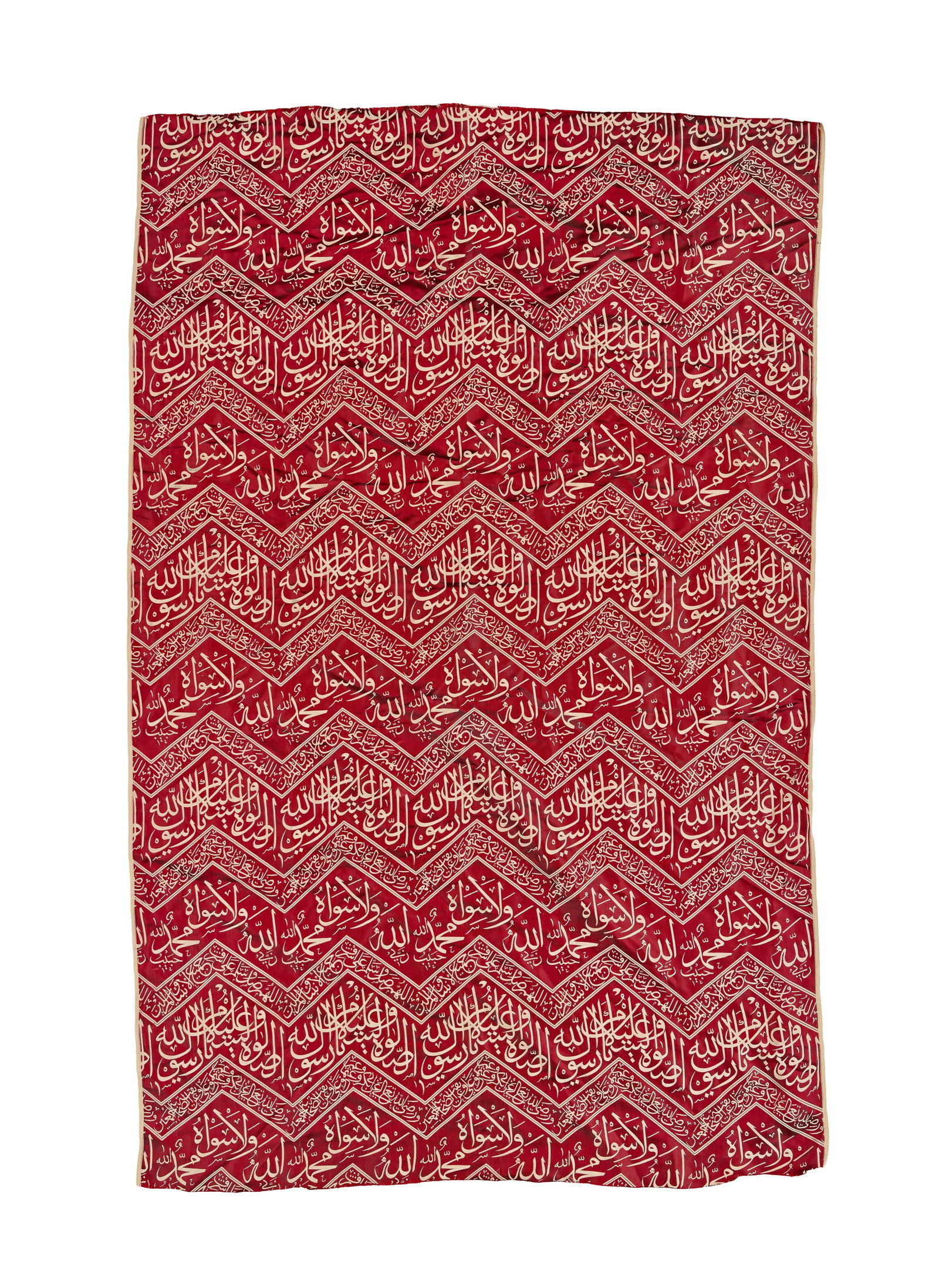 A RED-GROUND ISLAMIC CALLIGRAPHIC SILK TEXTILE, 20TH CENTURY: A rectangular woven silk lampas panel featuring a deep red ground with cream calligraphy and geometric borders. The design consists of continuous horizontal zigzag or chevron bands typical of imperial