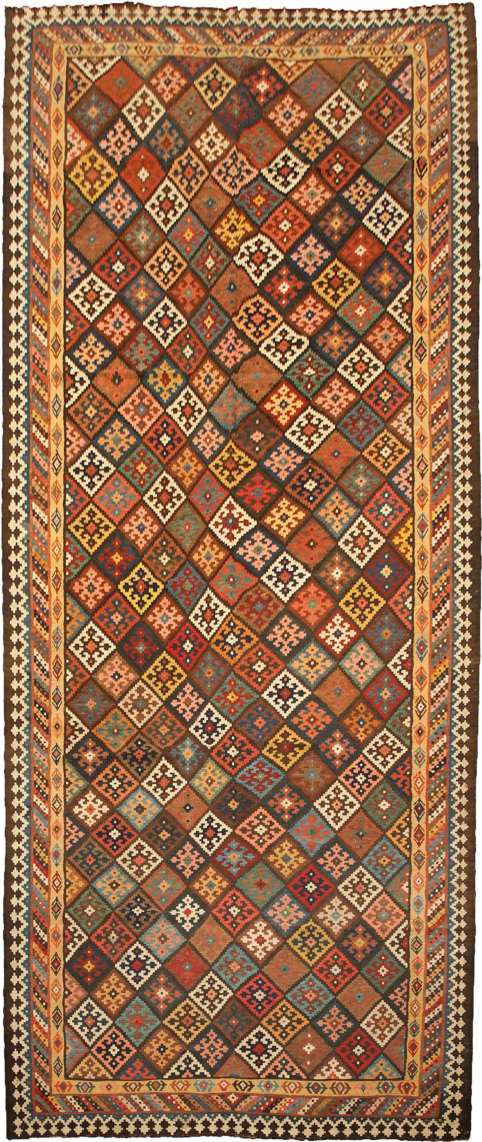 A LARGE BAKHTIAR KILIM CARPET, PERSIA, CIRCA 1900: A large hand-woven Bakhtiar kilim carpet dating to circa 1900. The rug features an all-over geometric design composed of a diagonal grid of polychrome lozenges. Each lozenge is filled with various tri