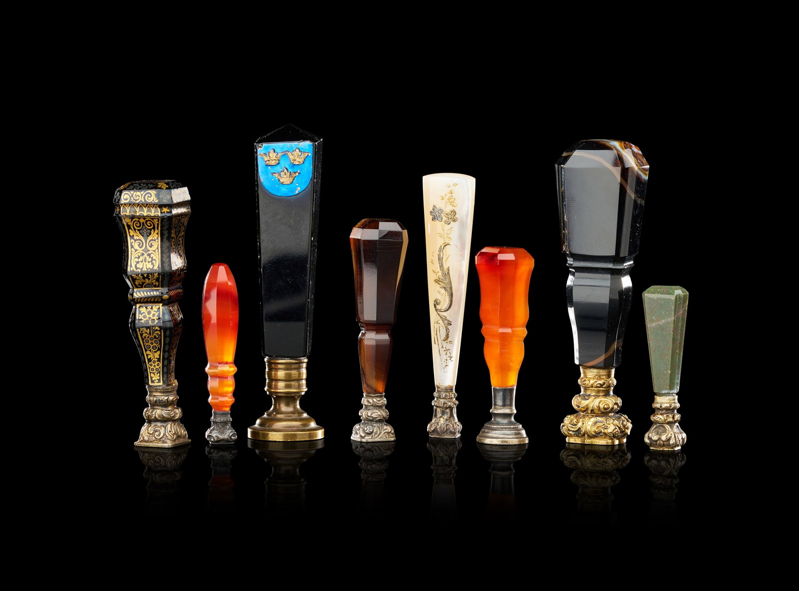 A COLLECTION OF EIGHT ANTIQUE HARDSTONE AND GILT-METAL DESK SEALS, 19TH CENTURY: A collection of eight individual nineteenth-century desk seals featuring various hardstone handles and metal mounts. The assortment includes handles fashioned from carnelian, banded agate, bloodstone,