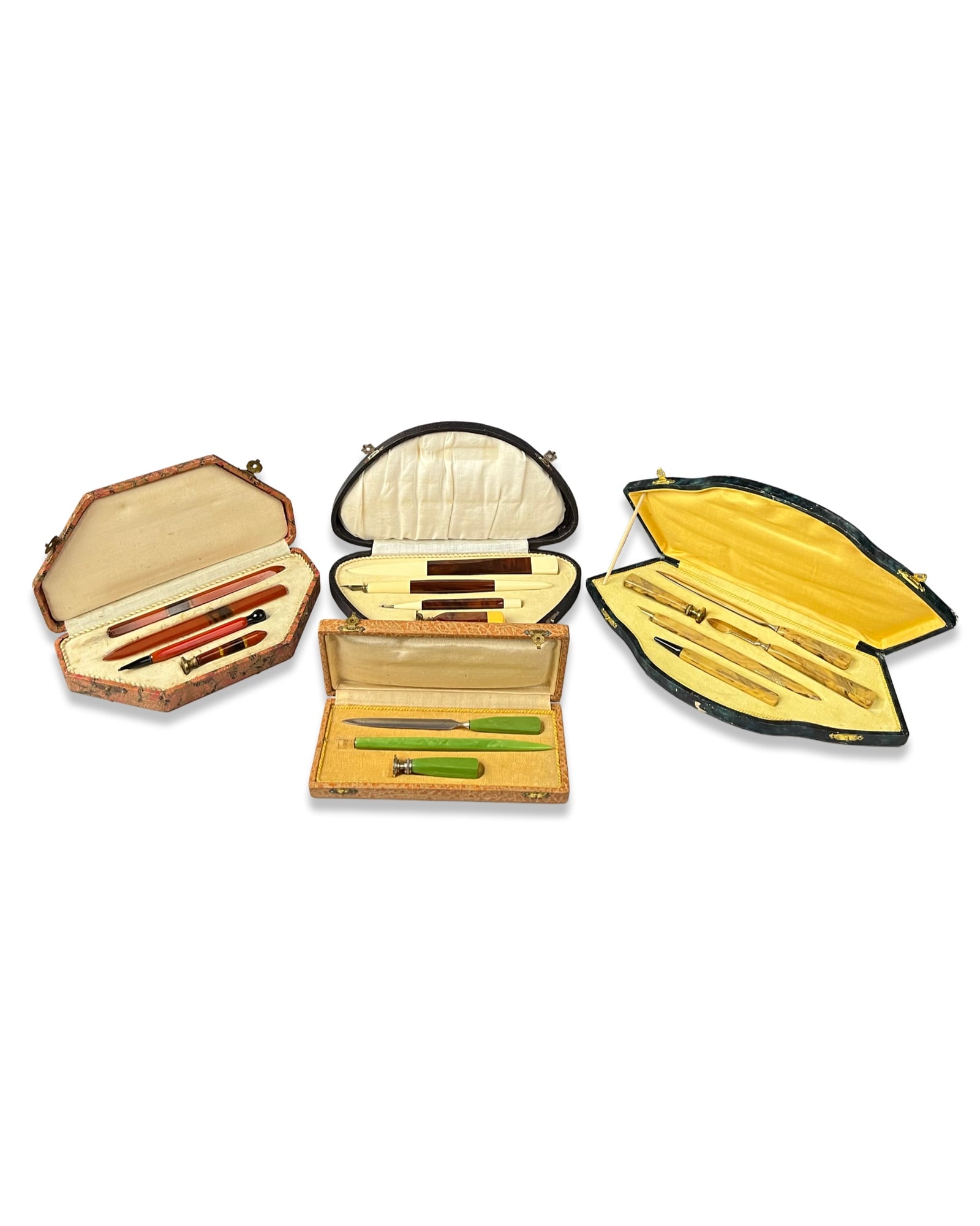 A COLLECTION OF ART DECO CASED CELLULOID DESK WRITING SETS WITH BAKELITE HANDLES: The collection includes a reddish-brown banded carnelian or agate set comprising a paper knife, a flat bookmark, a mechanical pencil with a black conical tip, and a wax seal with a circular brass matr