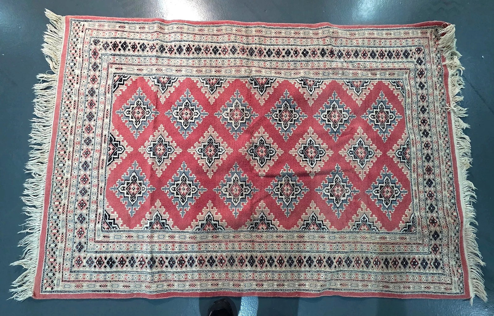 Ali Baba Cashmir Quality Bokhara Pattern Area Rug, 6 x 4 ft: An area rug featuring an allover stepped geometric diamond medallion pattern across a red ground, framed by repeating geometric borders and finished with fringed ends. An attached maker label on the