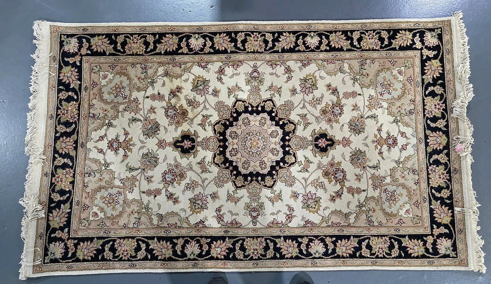 Persian-Style Floral Medallion Fringed Area Rug: A Persian-style area rug featuring an ivory-tone central field decorated with scrolling floral and vine motifs surrounding a multi-lobed central medallion in black, rose, and beige tones. The field