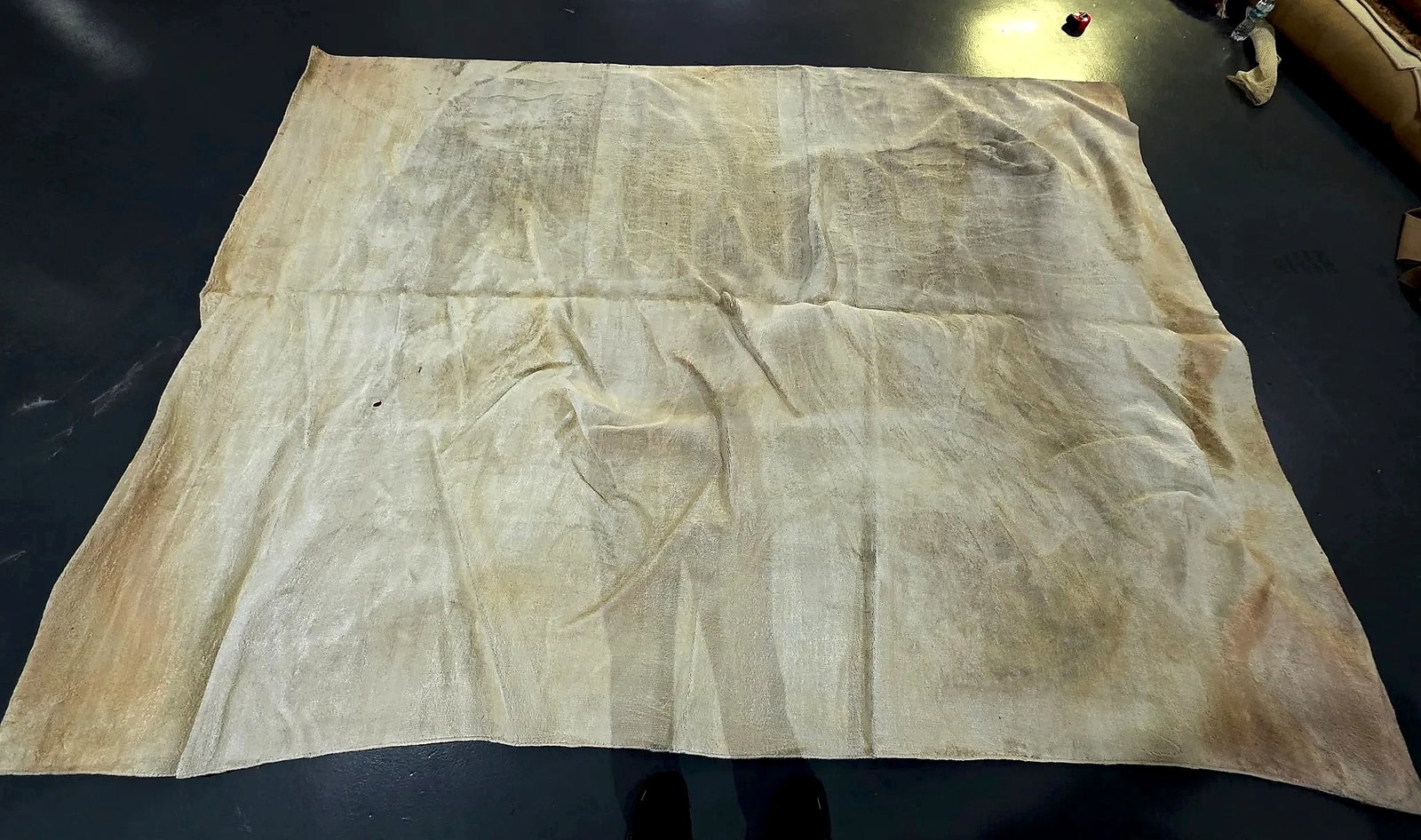Large Distressed Neutral-Tone Textile Ground Covering: A large rectangular textile ground covering or floor cloth featuring a variegated, mottled surface in neutral cream, beige, and tan tones. The surface shows visible folding creases, wrinkles,