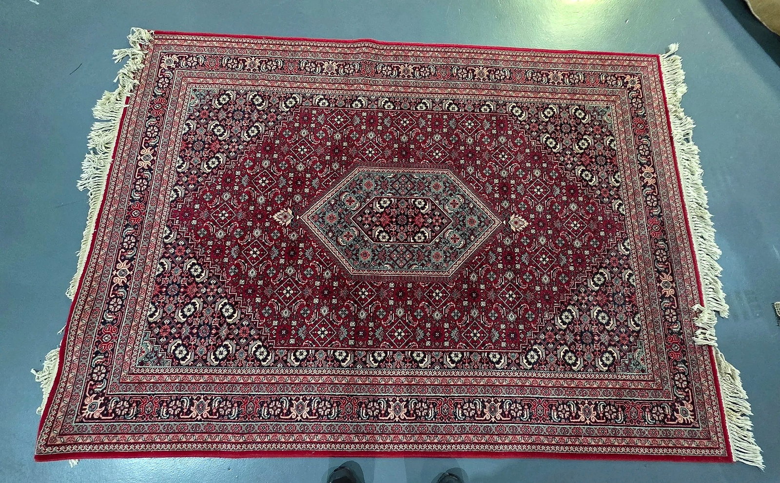 Persian Style Red Medallion Area Rug with Fringe: A Persian style area rug featuring a deep red ground filled with an allover repeating geometric and floral diamond lattice pattern. The composition is centered by an elongated hexagonal stepped