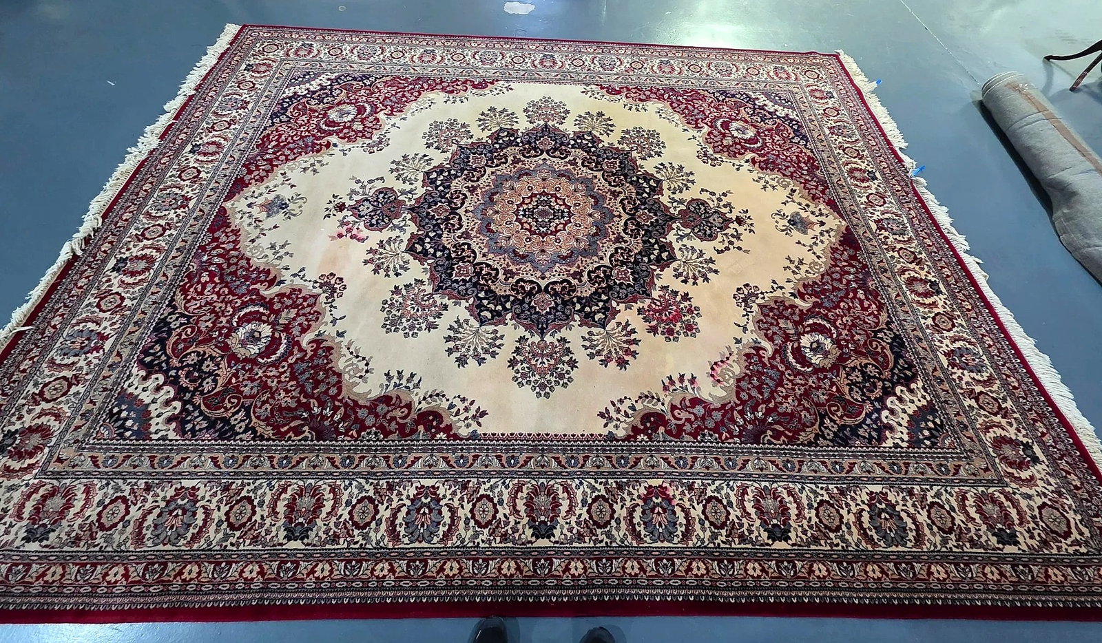 Persian-Style Floral Medallion Area Rug with Fringed Trim: Persian-style area rug featuring an ornate central floral medallion on a cream ground, framed by complementary burgundy red spandrels and multiple coordinating floral borders in navy, ivory, and red