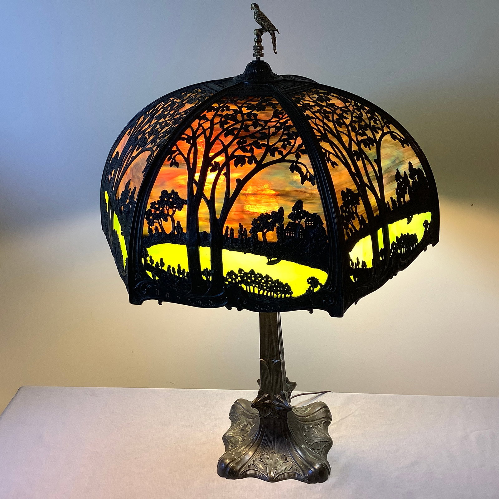 Antique Heavy Bronze Large Slag Glass Lamp: 6 top curved glass panels behind a filigree design consisting of tree in foreground and countryside in background Small lower glass panels appear to be a small pond framed with small foliage Lower sla