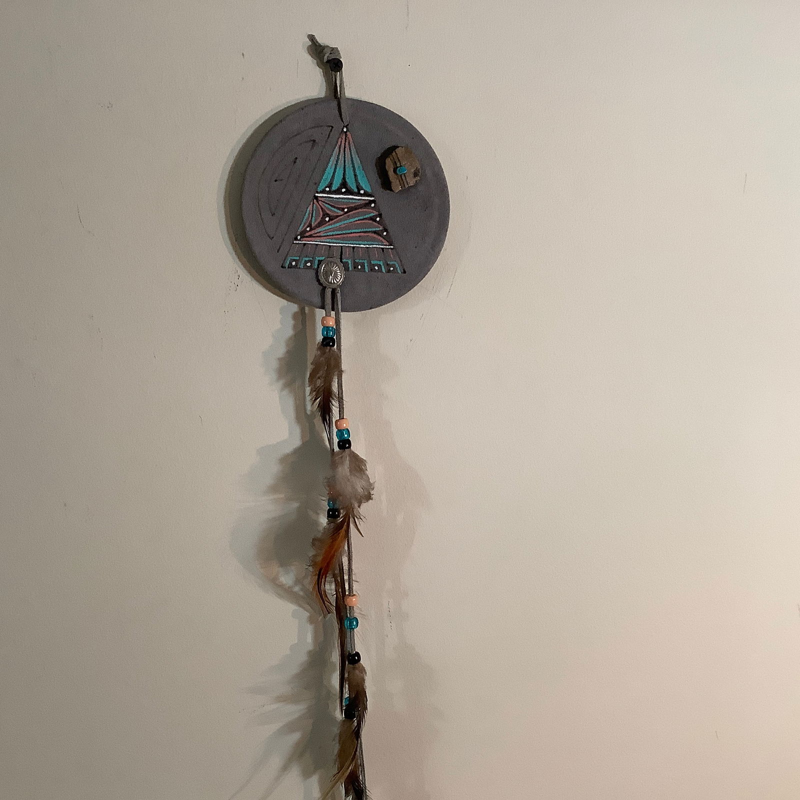 Small Alaskan Native American Painted Leather Medicine Shield with Stones: Shield made of suede leather with painted design, stone and turquoise piece Long leather beaded and feather cord hangs from concho Signed on back