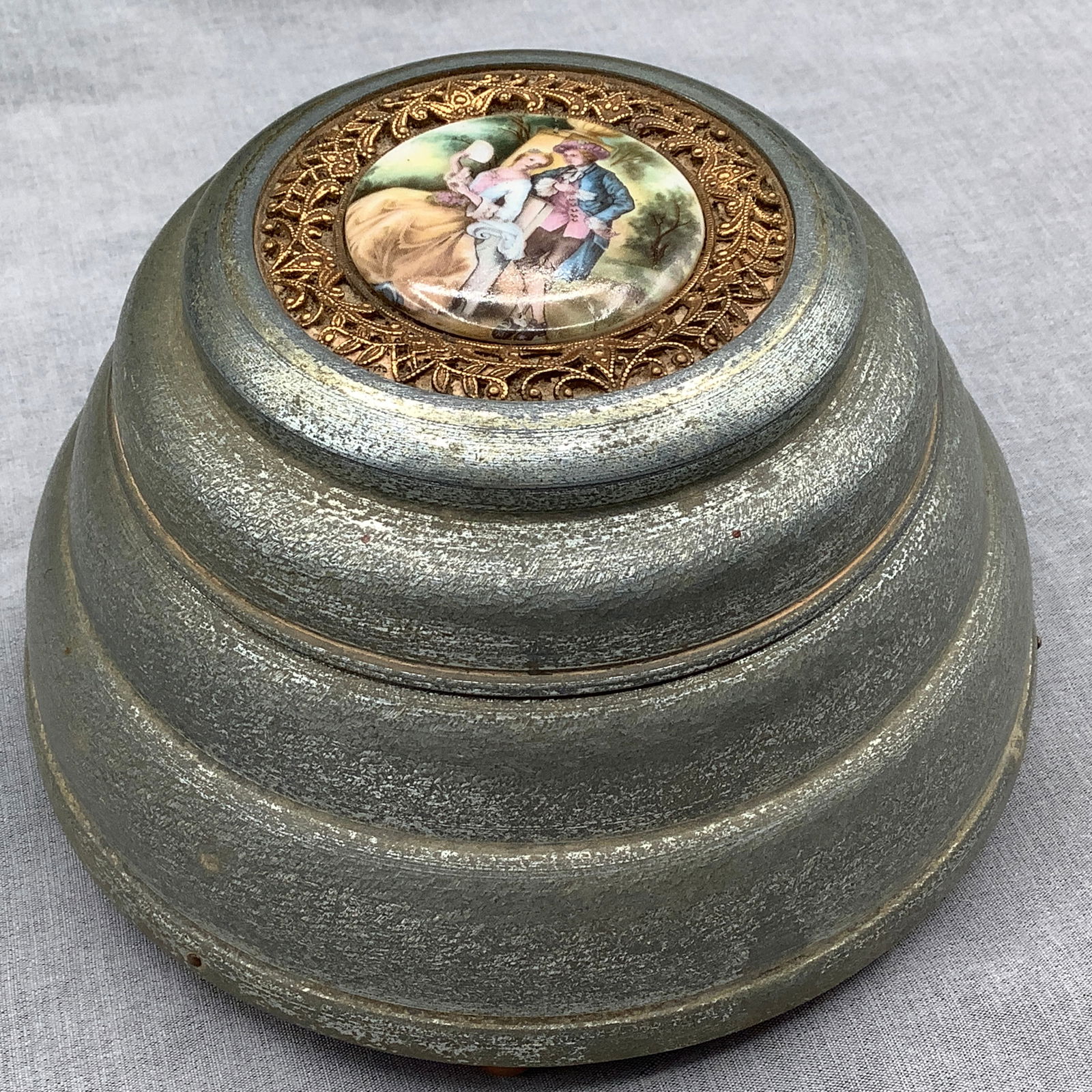 Antique 1920s Aluminum Powder Puff Music Box, Works: Works wonderfully Has Victorian scene on top of lid with brass filigree border