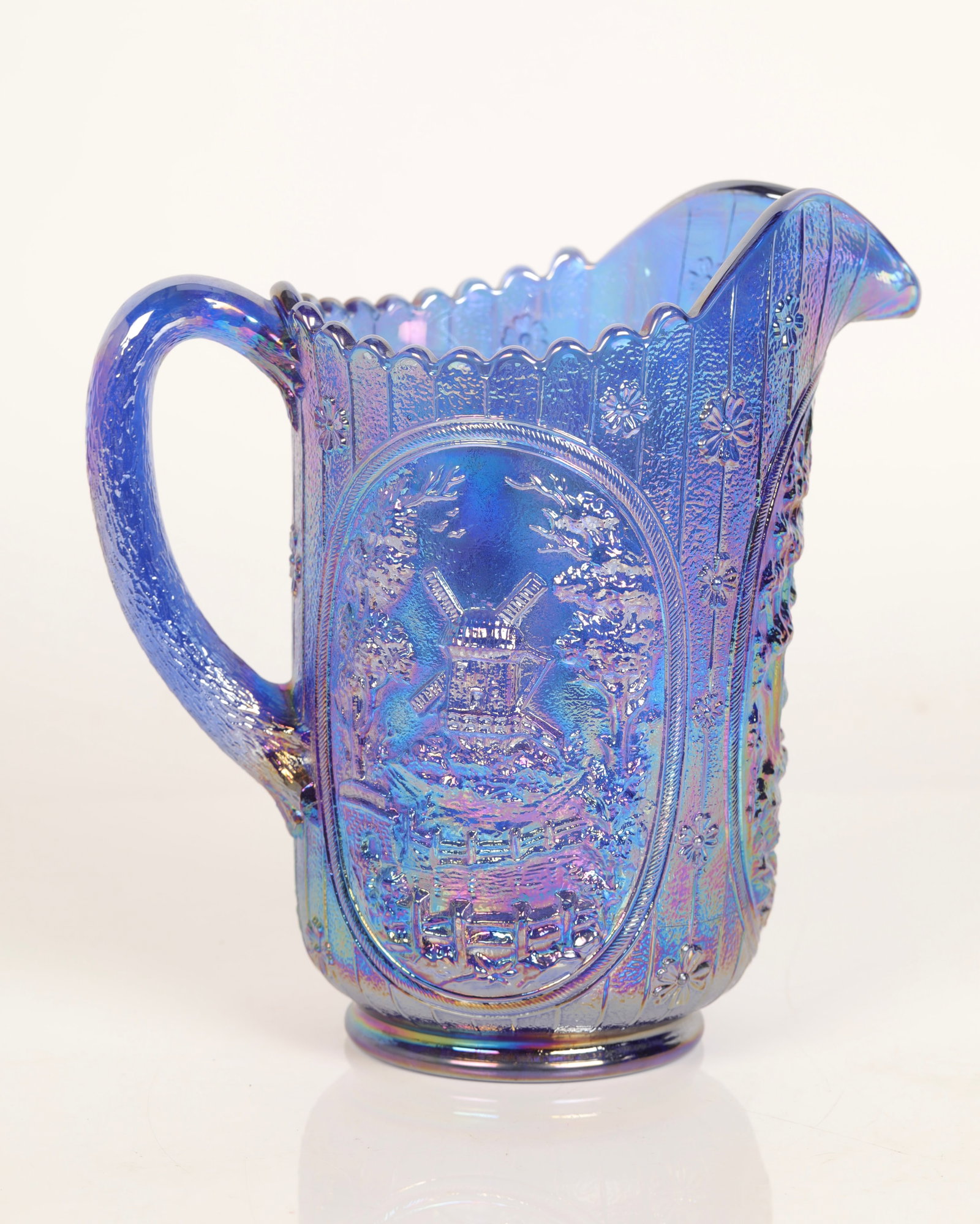 CARNIVAL GLASS PITCHER DUTCH WINDMILL IMPERIAL: A carnival glass pitcher with Dutch windmill scene. Made by Imperial glass. 8.5" H x 5" diameter x 9" wide (handle to spout)