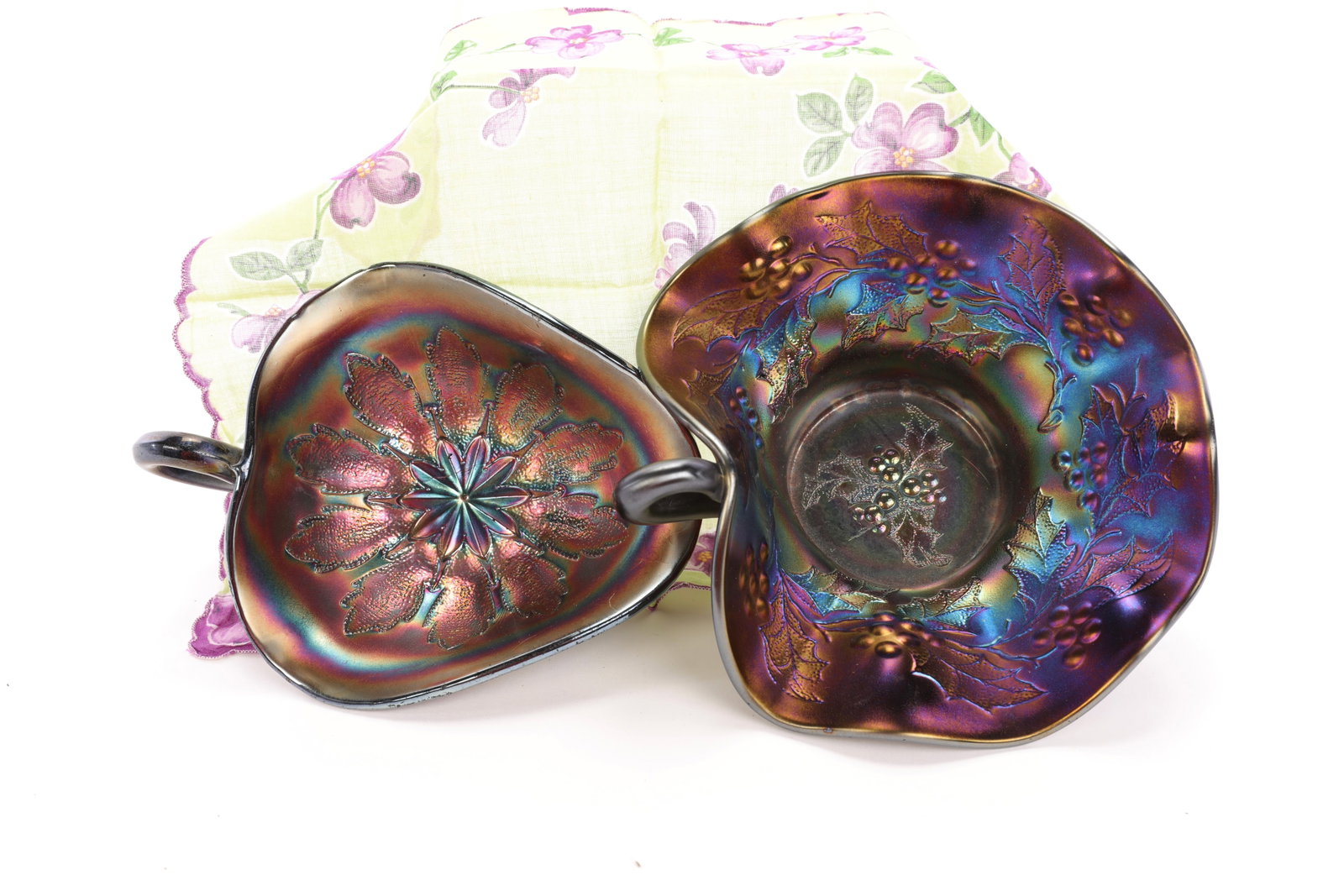 2 PURPLE CARNIVAL GLASS NAPPY DISHES HOLLY BERRY & LEAF: A pair of purple iridescent carnival glass nappy dishes. One has holly & berry relief and the other has a leaf & star pattern. Holly: 3.5" x 7" Leaf: 2.5" x 7"