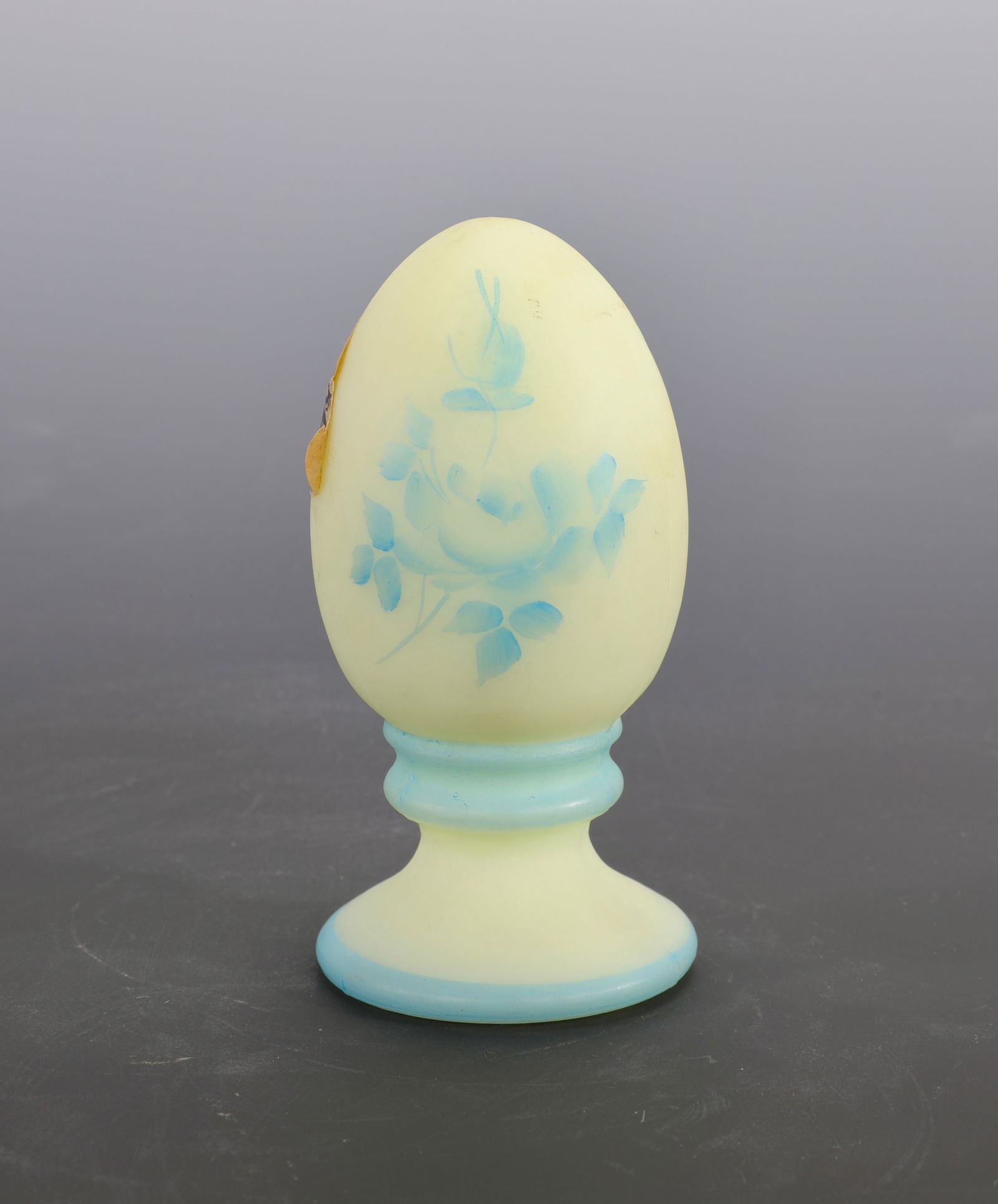 FENTON CUSTARD GLASS EGG ON BASE UV REACTIVE HAND PAINTED: A lovely Fenton custard glass egg on attached base. It is hand-painted and UV reactive; it glows under a black light. Signed on the base. Retains original Fenton sticker label.Measures: 3" h x 1.5" W