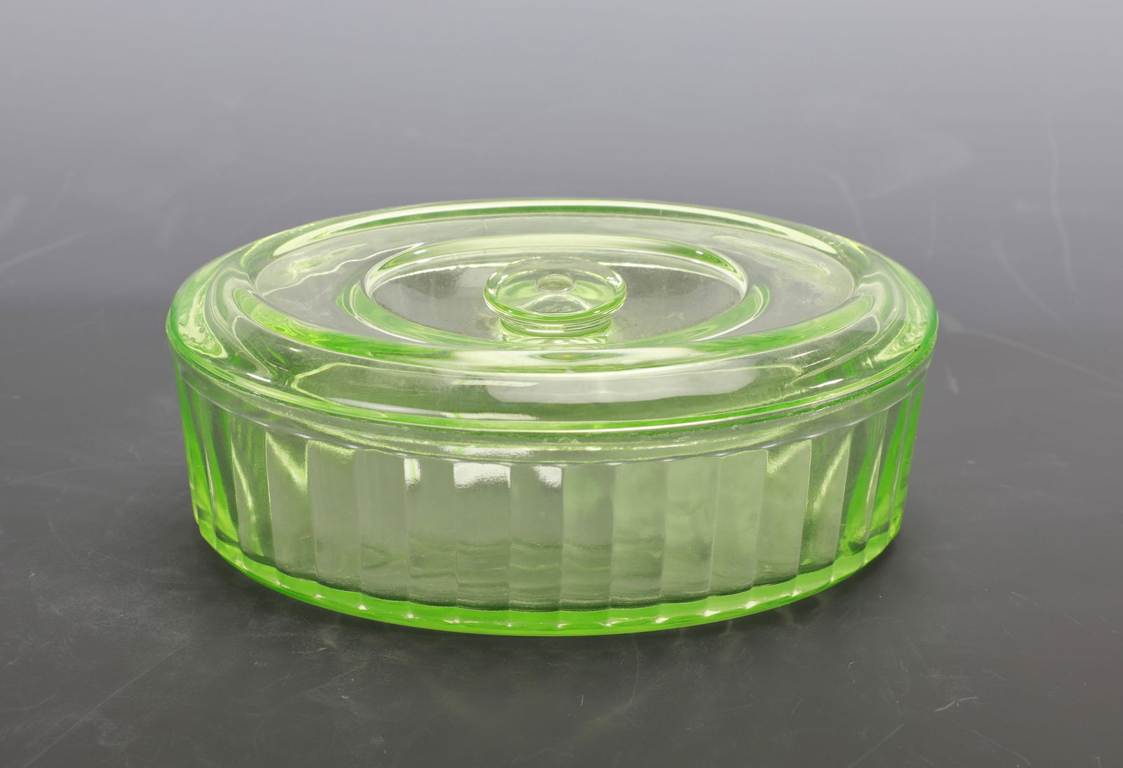 GREEN URANIUM GLASS REFRIGERATOR LIDDED CASSEROLE DISH: A green uranium glass lidded casserole or refrigerator dish. It features ribbed sides and a lidded handle. Measures: 2.5"H x 6" W INV#- Lime green 15