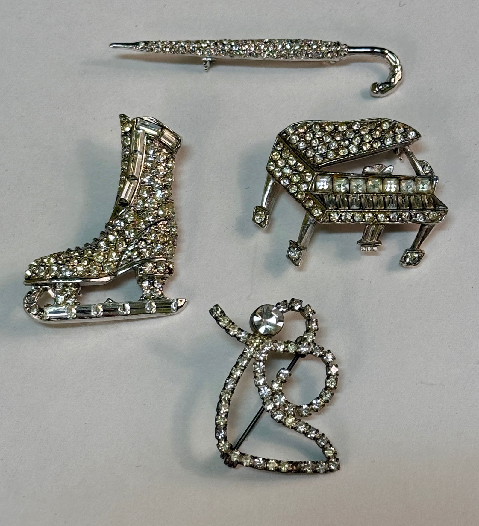 Group of Four Costume Jewelry Pins Brooches Figural Clear Rhinestones: From an upstate, NY estate collection. Group of four vintage 1940s-80's rhinestone figural pins / brooches. Grand piano, ice skate (marked Pell), folded umbrella, and angel.