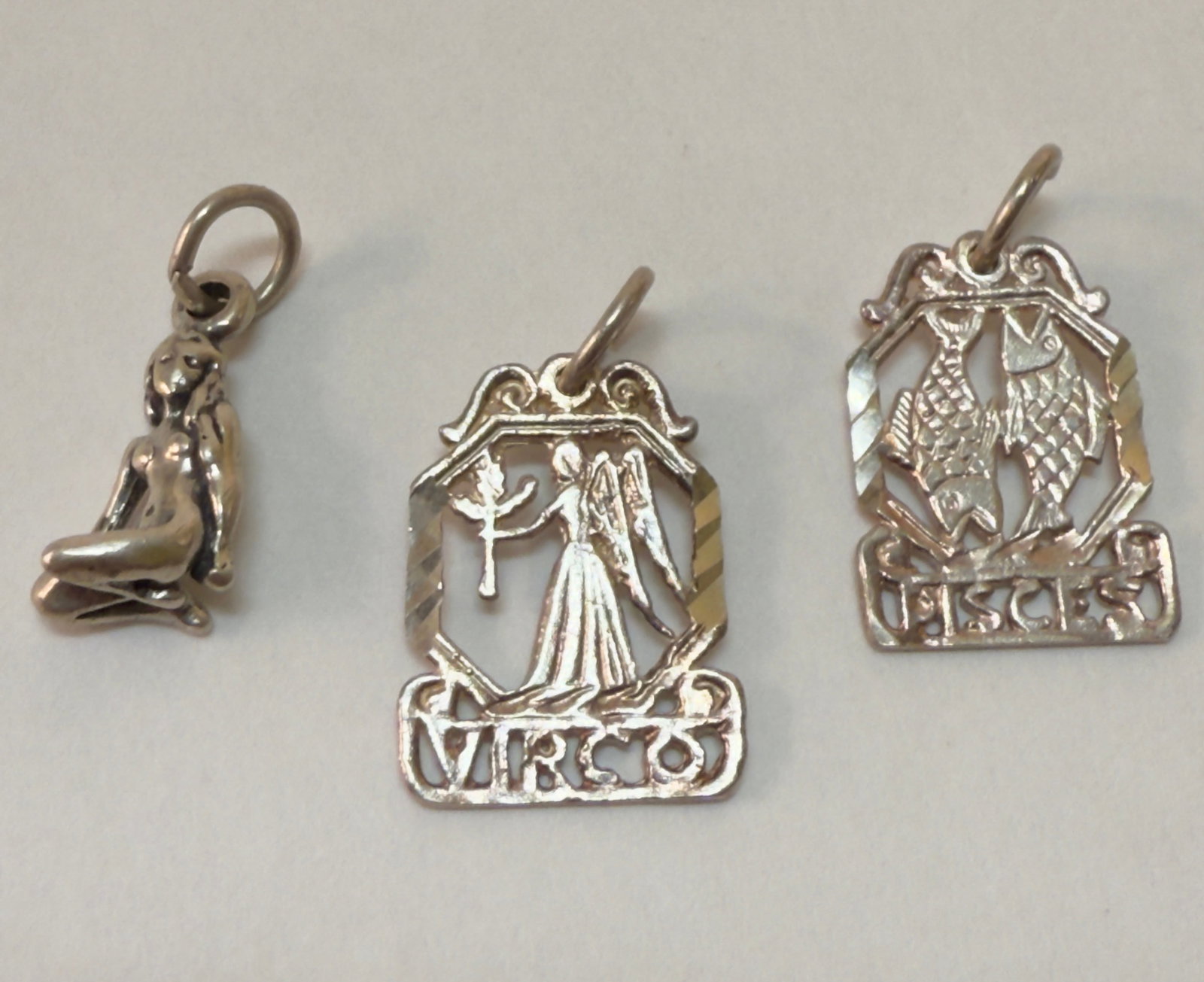Group of Three Vintage Sterling Silver Charm Bracelet Charms - Zodiac, Nude Figure: From an upstate, NY estate collection. Group of three vintage sterling silver charms including two zodiac charms (Pisces & Virgo) and one seated nude female figure. Zodiac charms both marked 925, all 