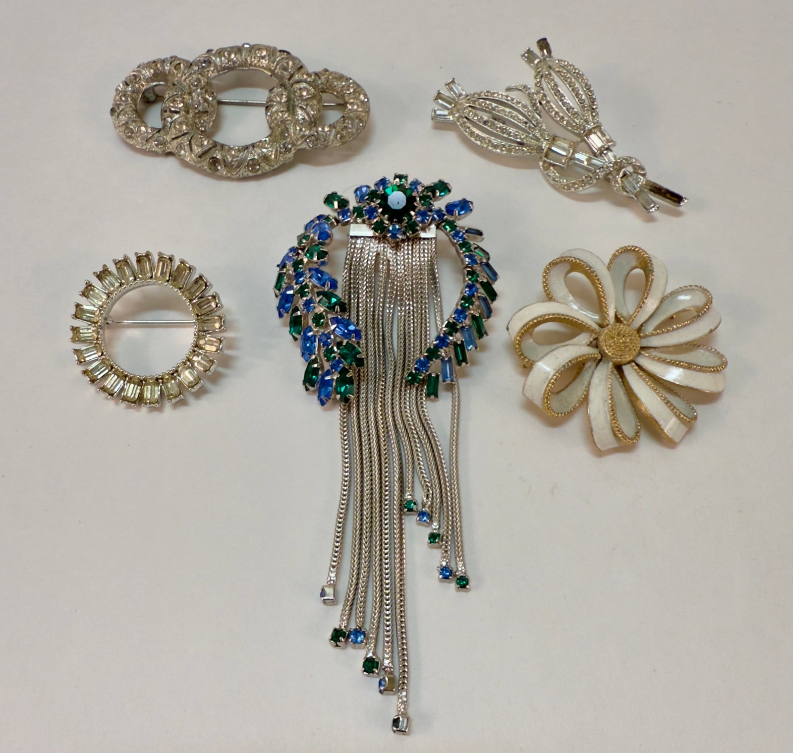 Group of Five Vintage Rhinestone Brooches, Pendants Trifari +: From an upstate, NY estate. Group of four vintage rhinestone and enamel pins or brooches, and one silver tone fringed rhinestone flexible pendant. White enamel brooch is signed Trifari.