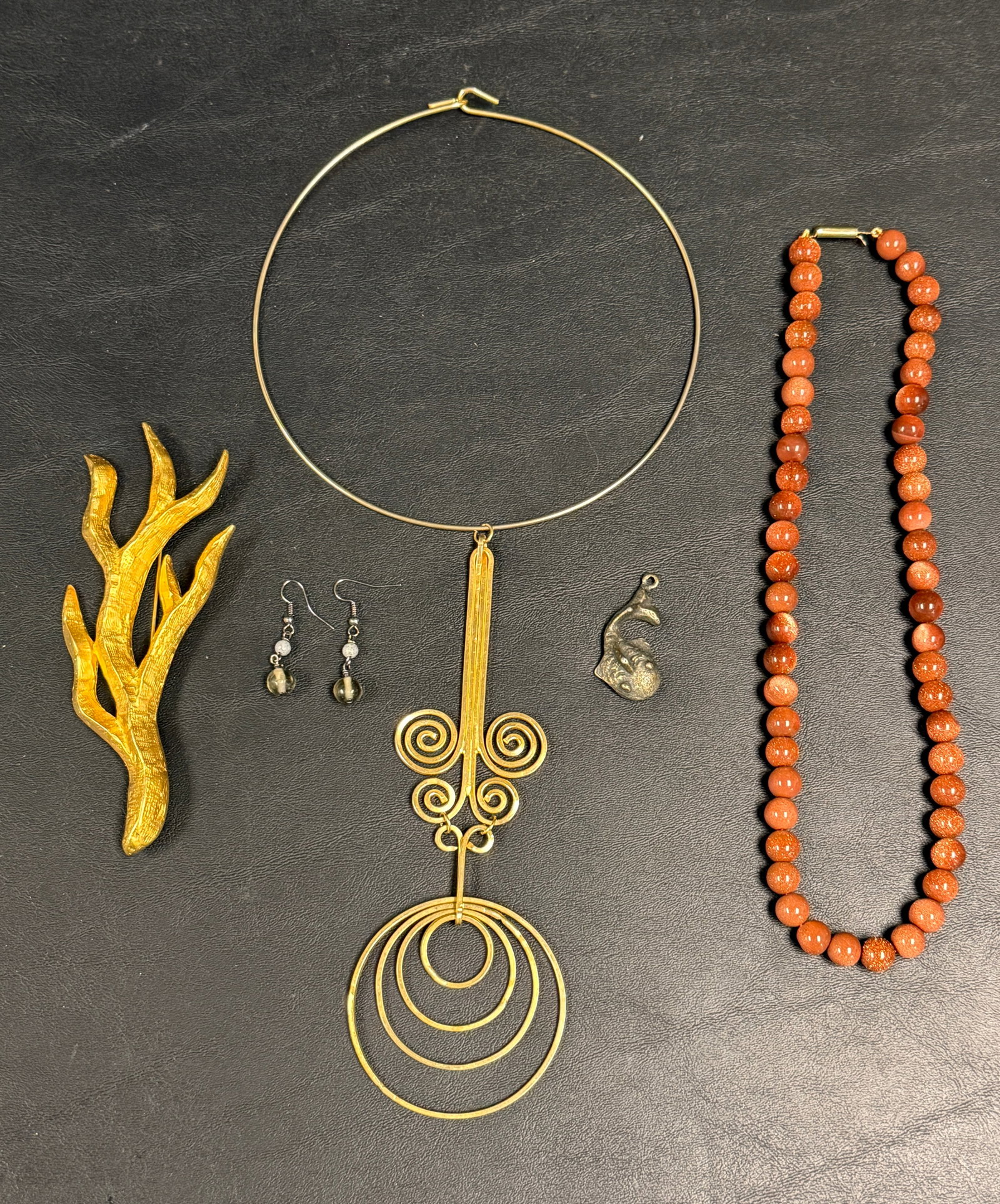 Group of 5 Vintage Jewelry Pieces Goldstone Beads +: From an upstate, NY estate. Vintage group of five jewelry pieces, including metal fish charm, goldstone beaded necklace, artisan gold tone goddess choker necklace, pair of semi-precious stone beaded