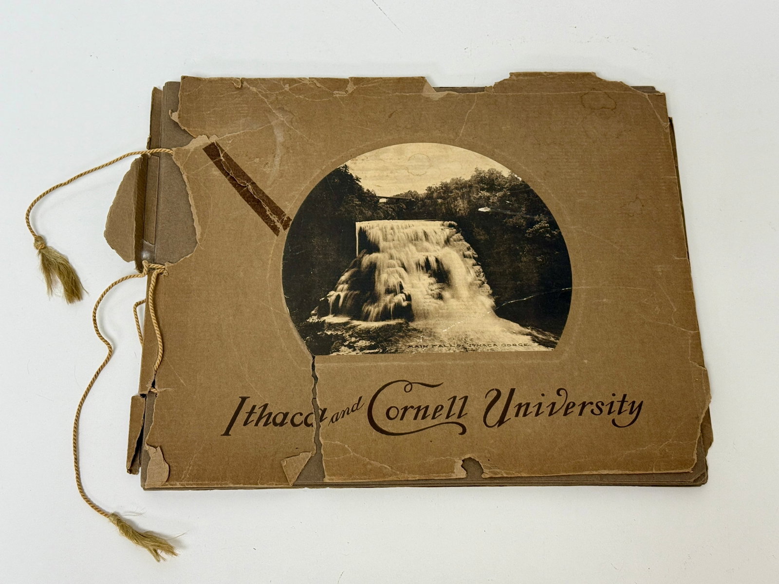 Early 20thC Photogravure Souvenir Book Ithaca and Cornell University: From an upstate, NY estate. Rare photogravure souvenir book of Ithaca & Cornell University. Ealy 20thC. Book measures approx 12.5" x 10.25". Cover as significant tear. String binding is coming undone.