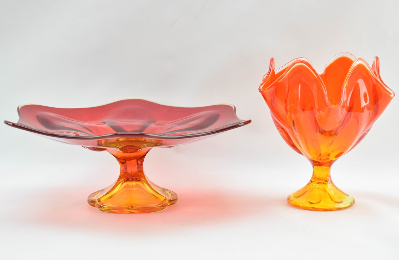 Two Vibrant Orange Glass Dishes: Includes one Danish cake stand in red and tangerine tones and one serving goblet with a petal rim and an ombre stem. Both feature elegant indents in the glass and organic, curved designs.