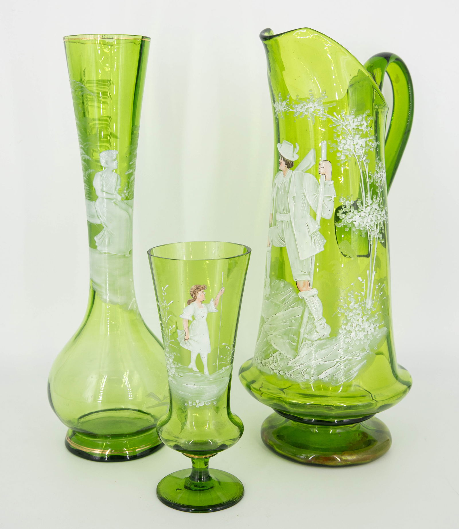 Three Antique Victorian Mary Gregory Green Glass Vessels: Three Mary Gregory enameled Victorian glass pieces, including one tall fluted vase with a depiction of a woman seated by a lake, a small footed vase with a depiction of a girl holding a tall reed, and