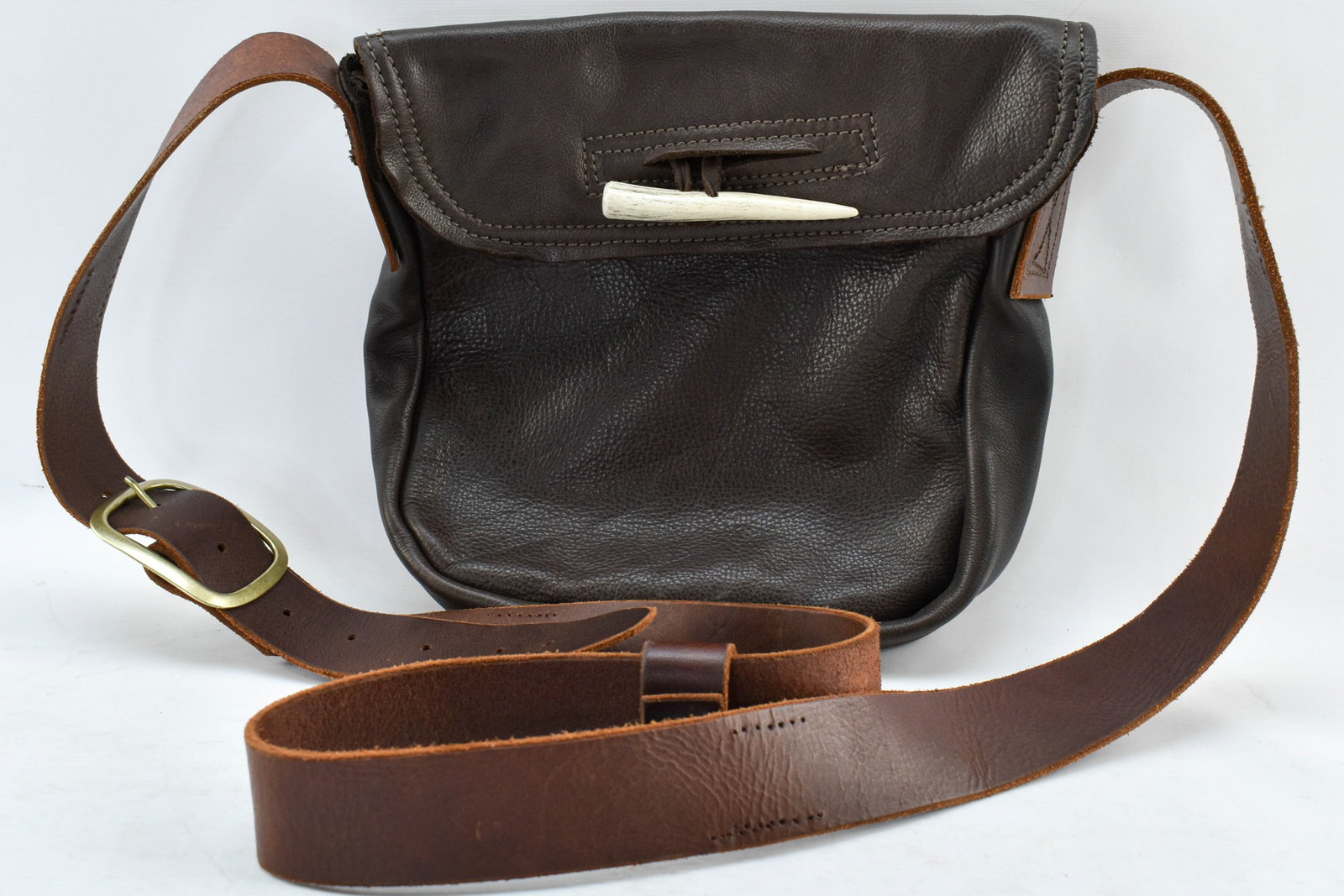 Handmade Leather Crossbody Bag with Tusk Clasp: Pebbled leather crossbody purse with a thick adjustable strap, interior pockets including pen holders, and a clasp that appears to be a small animal tusk or reproduction thereof. No brand indications,