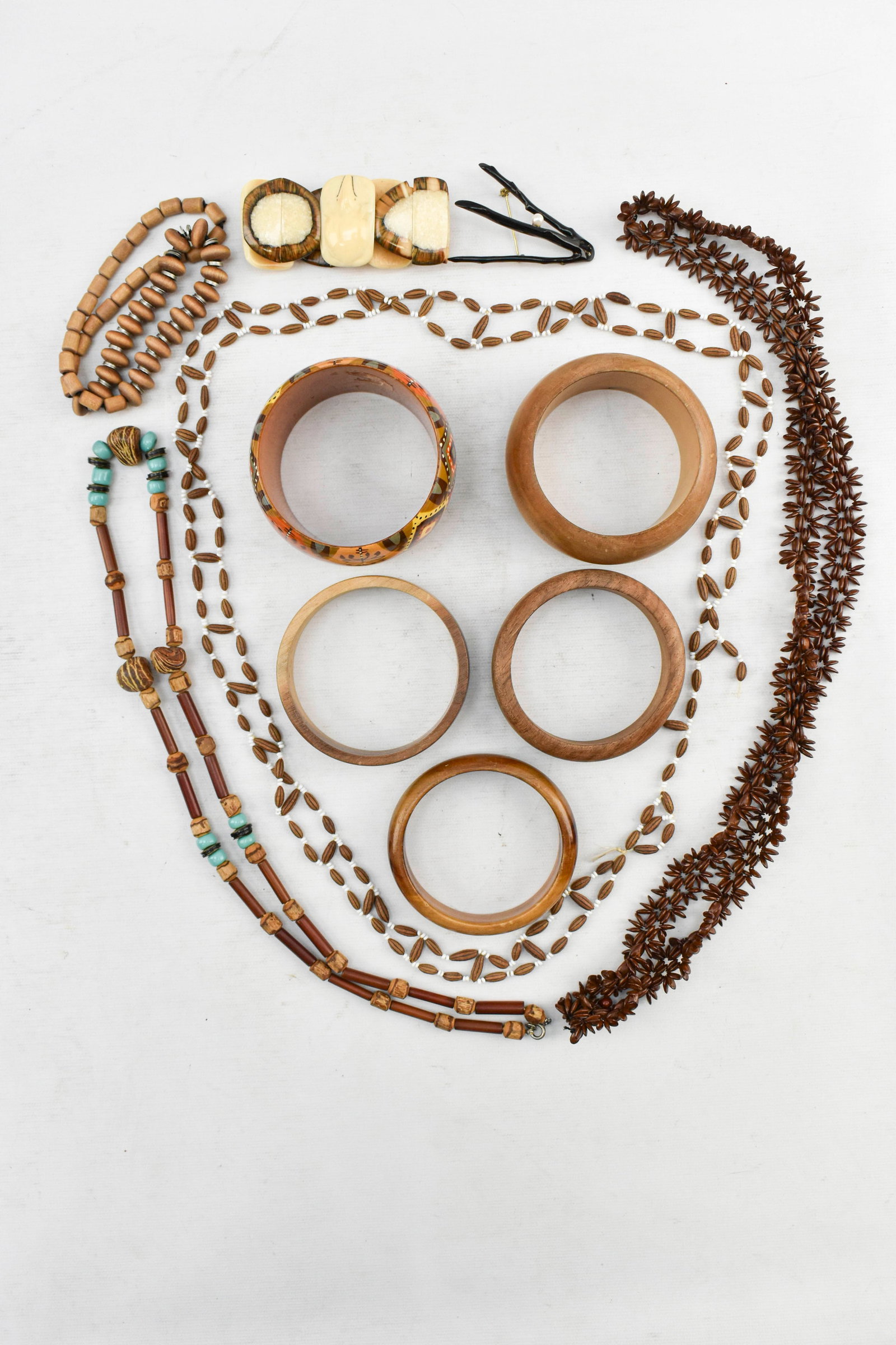 Group of Wood and Coral Jewelry: Assortment of eclectic jewelry including wooden bangles, beaded necklaces, a bangle with carved animal figures on what appears to be bone, a rare Royal Hawaiian Black Coral pin with a cultured pearl i