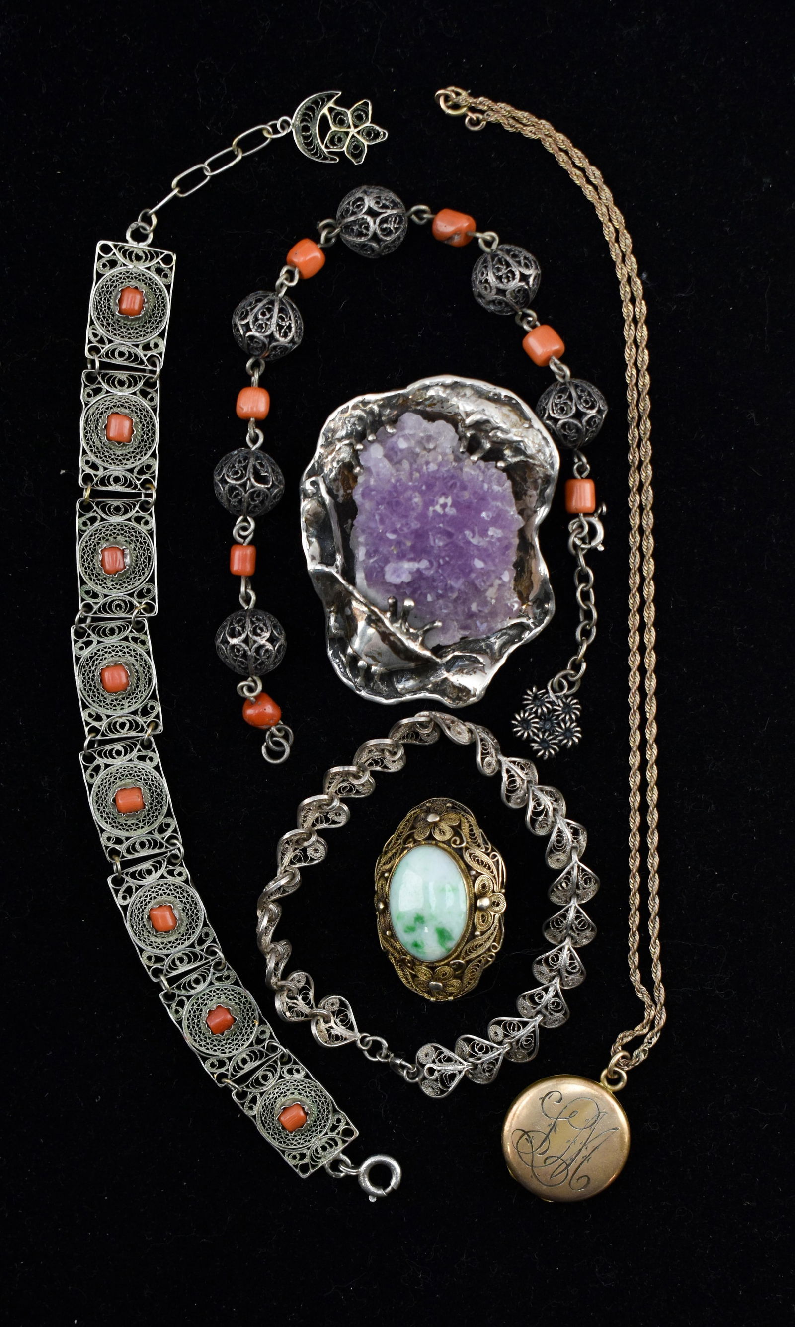 Group of Silver and Silver-Tone Jewelry: Includes a geode brooch, a filigree spinach jade brooch, an empty locket with the initials LM monogrammed on the outside and the number 67 etched on the interior, a pin that appears to be inlaid mothe