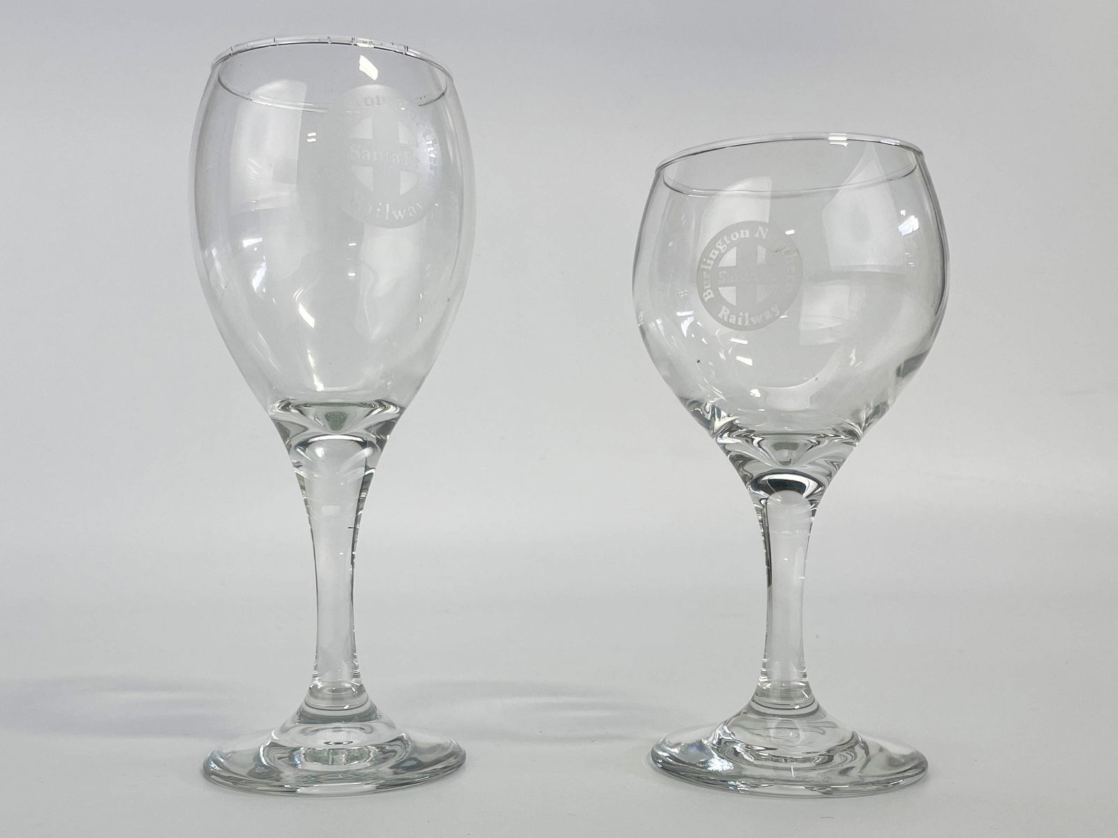 2 Burlington Northern Railway Stem Wine Glasses: Group of two glass wine goblets with clear stems. Etched "Burlington Northern Railway Santa Fe" along the side.7.25 x 3.25 x 3.25