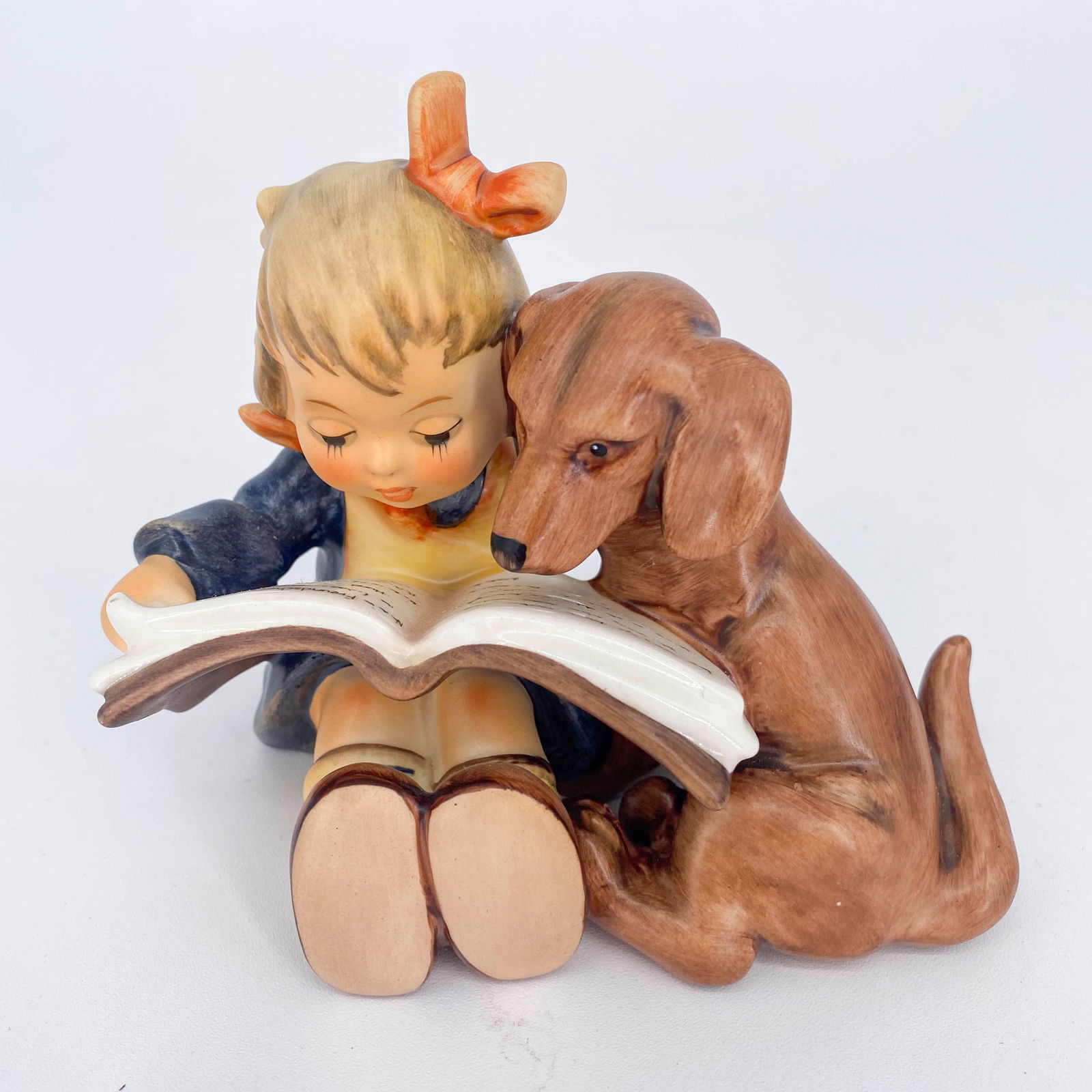 Goebel Hummel Proud Moments Figurine 800: Ceramic figurine by Goebel Hummel titled Proud Moments depicting a little girl reading to her dog. Marked on underside with Goebel logo. Sticker adhered to back and signed on back. Marked 800 on under
