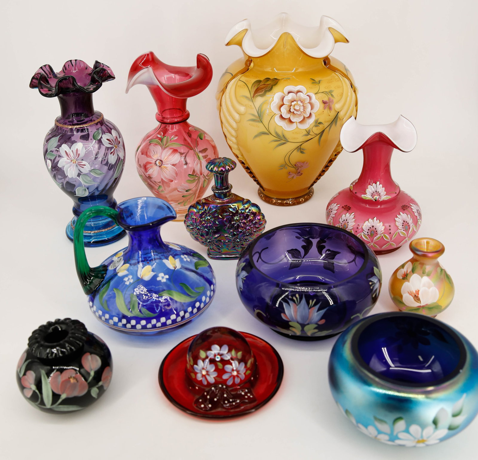 Lot of 11 Hand Painted Fenton Glass Vessels: Assortment of 10 handpainted (and one unpainted) vessels including a small pitcher, several vases, bowls, and more. Most are signed/marked on the underside. Largest: 9 1/8"H x 7"W x 6 1/8&qu